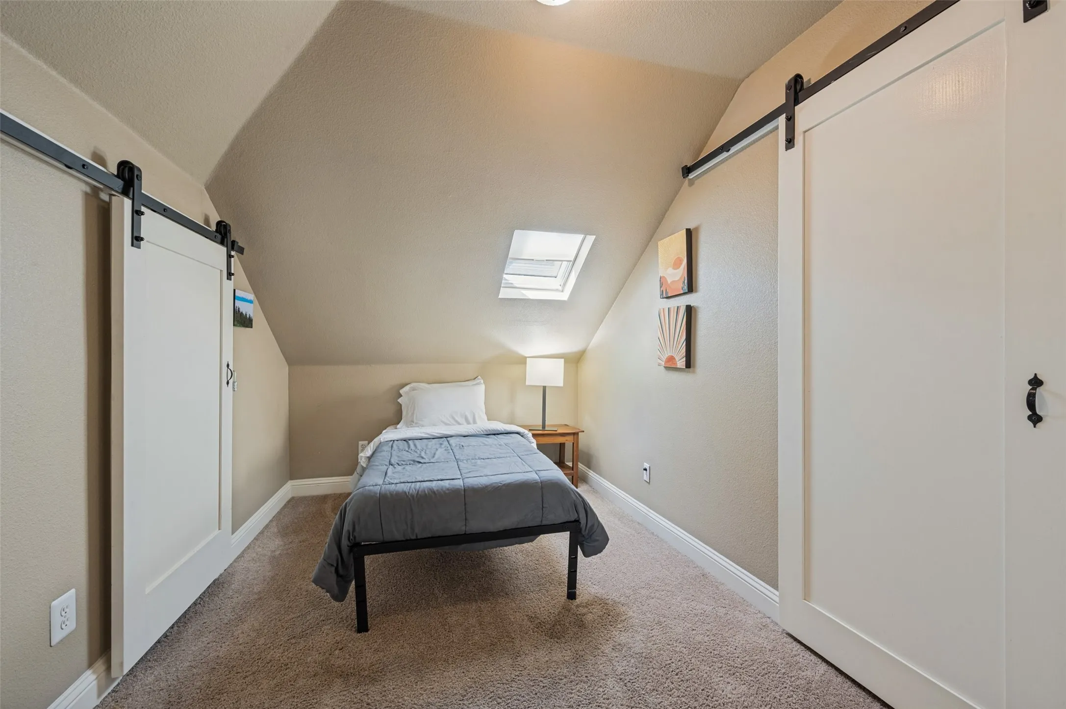 Sloped ceilings with a skylight, barn doors with black hardware, and wall-to-wall carpeting
