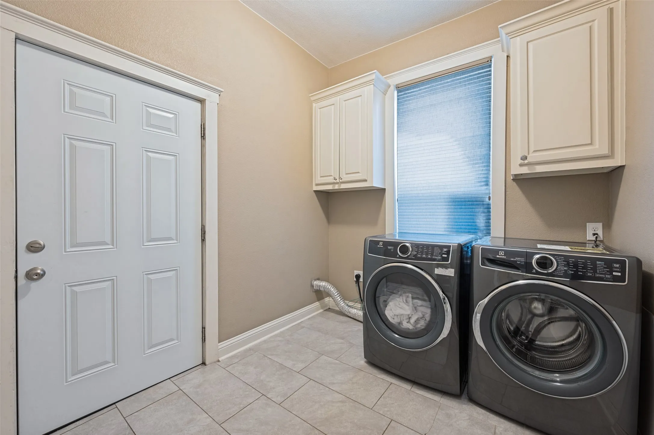 Recessed panel door with brushed nickel hardware, light tile flooring, built-in cabinetry, and a window with blinds