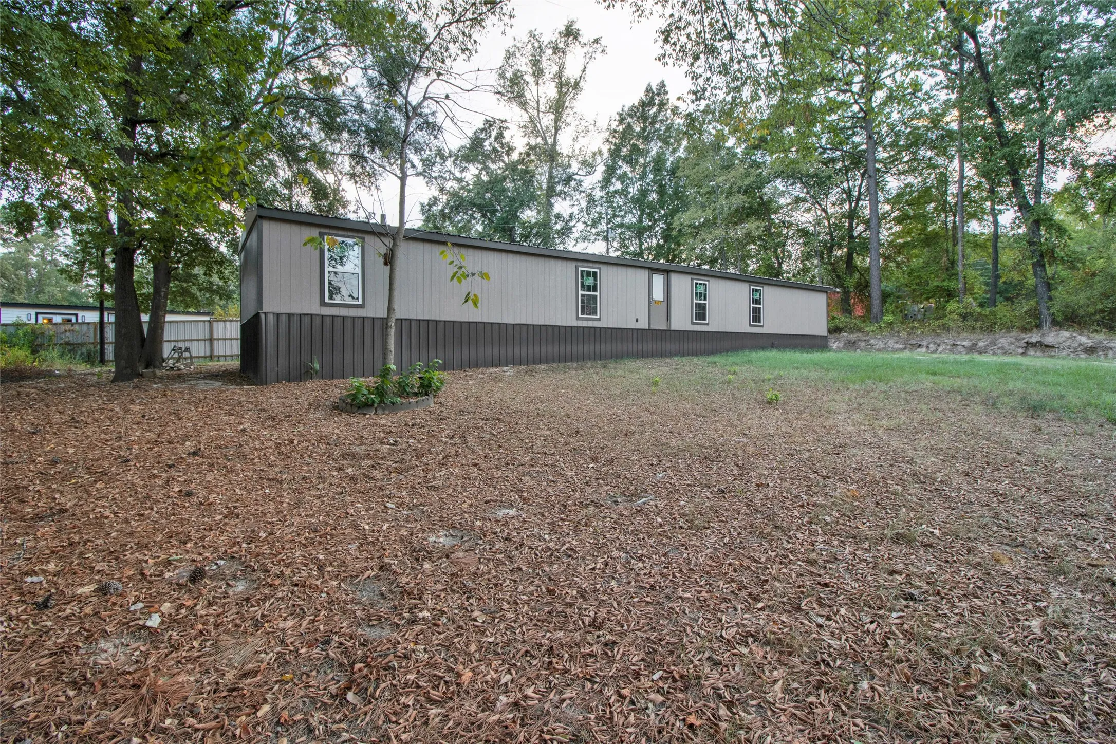 Single-story structure with two-tone siding, multiple windows, and surrounding mature trees