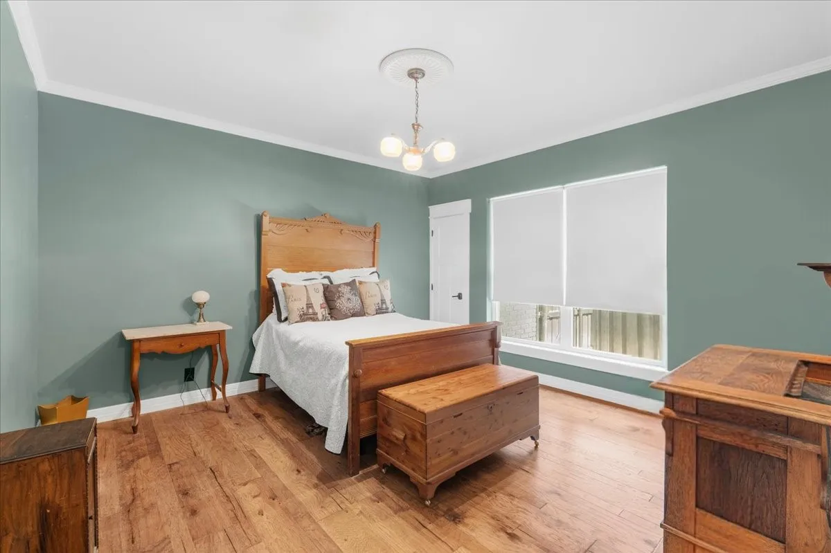 Hardwood-finish flooring, crown molding, double window with roller shades, and a ceiling-mounted light fixture