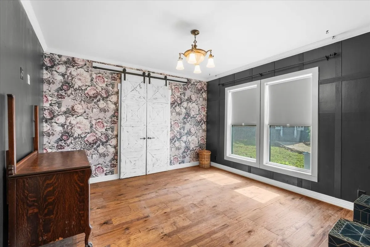Hardwood flooring, decorative wall paneling, dual windows, ceiling-mounted lighting fixture, and barn doors