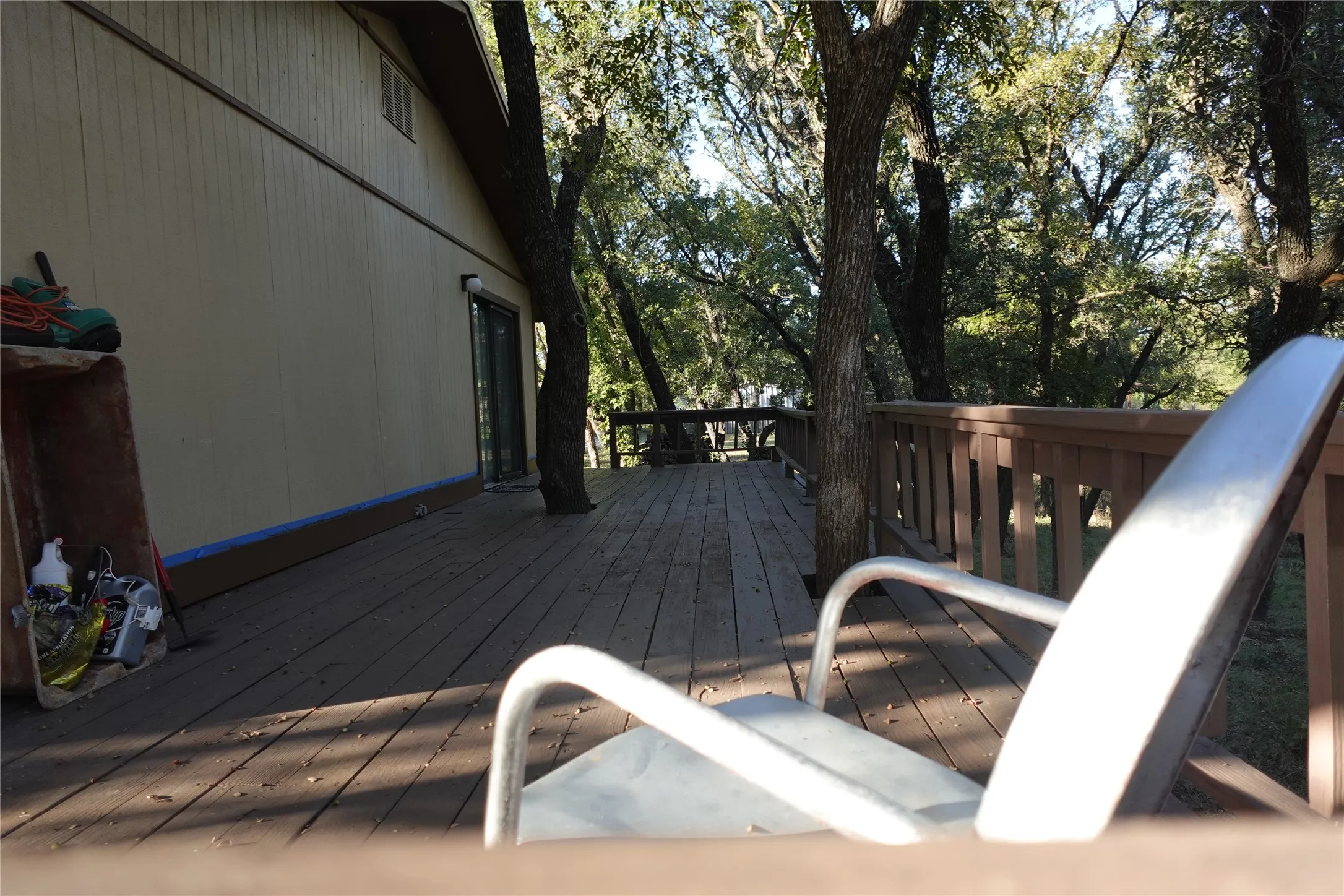 Expansive wood deck with a built-in railing, surrounded by mature trees, and featuring a sliding glass door entry to the property