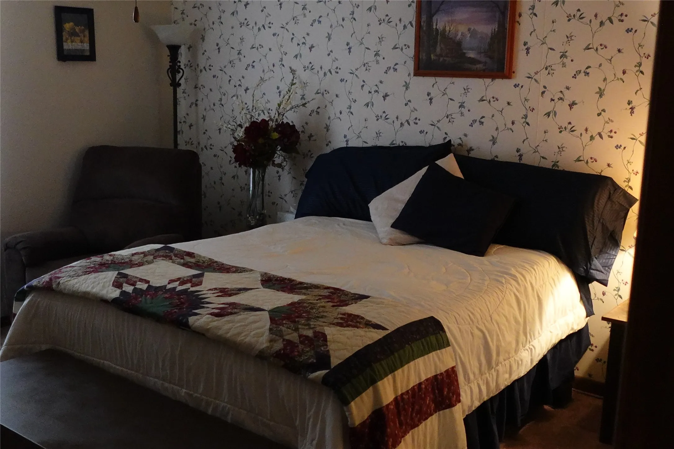 Wallpapered accent wall with a botanical pattern, dark wood-finish side table, and a floor lamp with a white glass shade