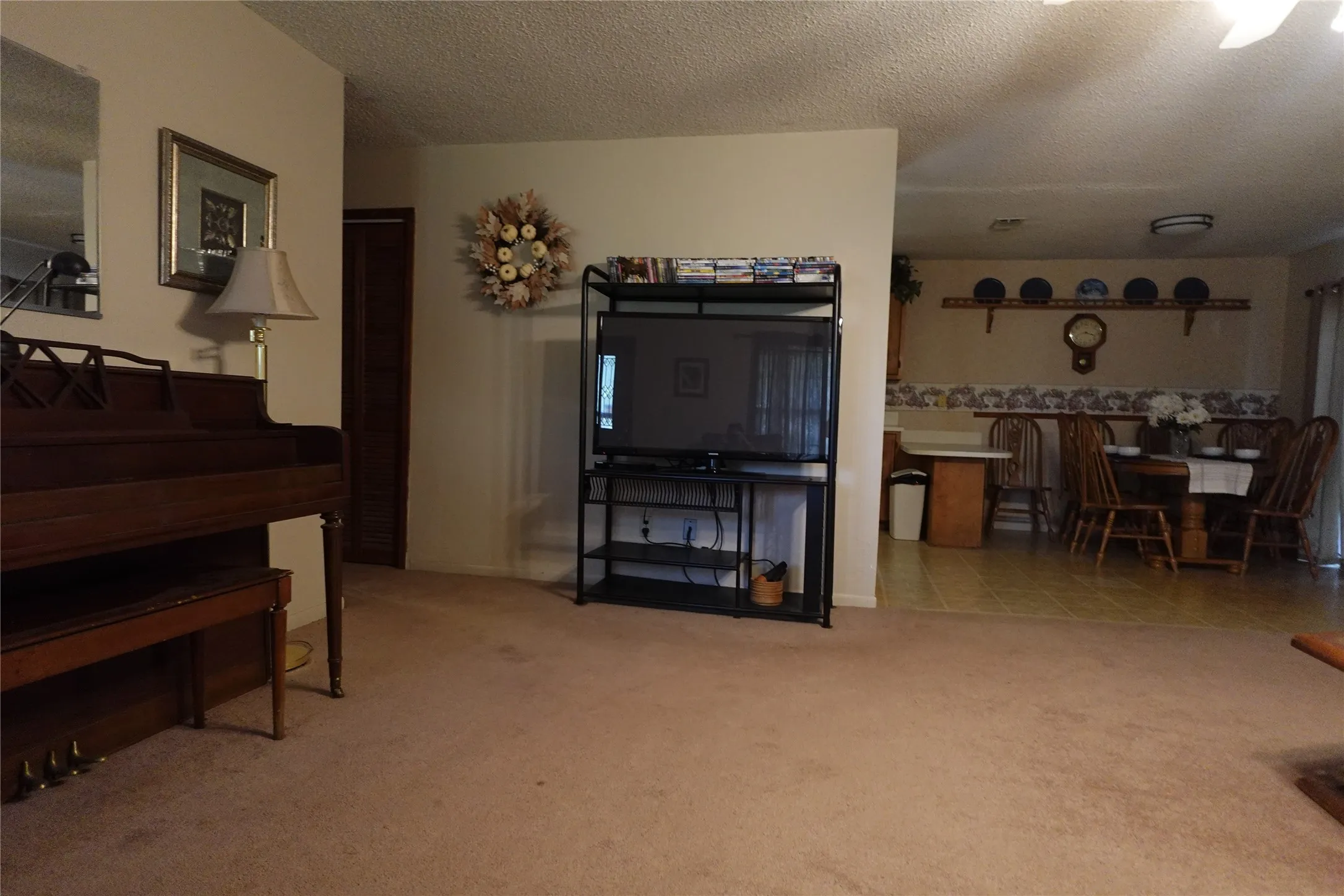 Carpeted living area with textured ceiling, leading to a dining area featuring wood-finish flooring