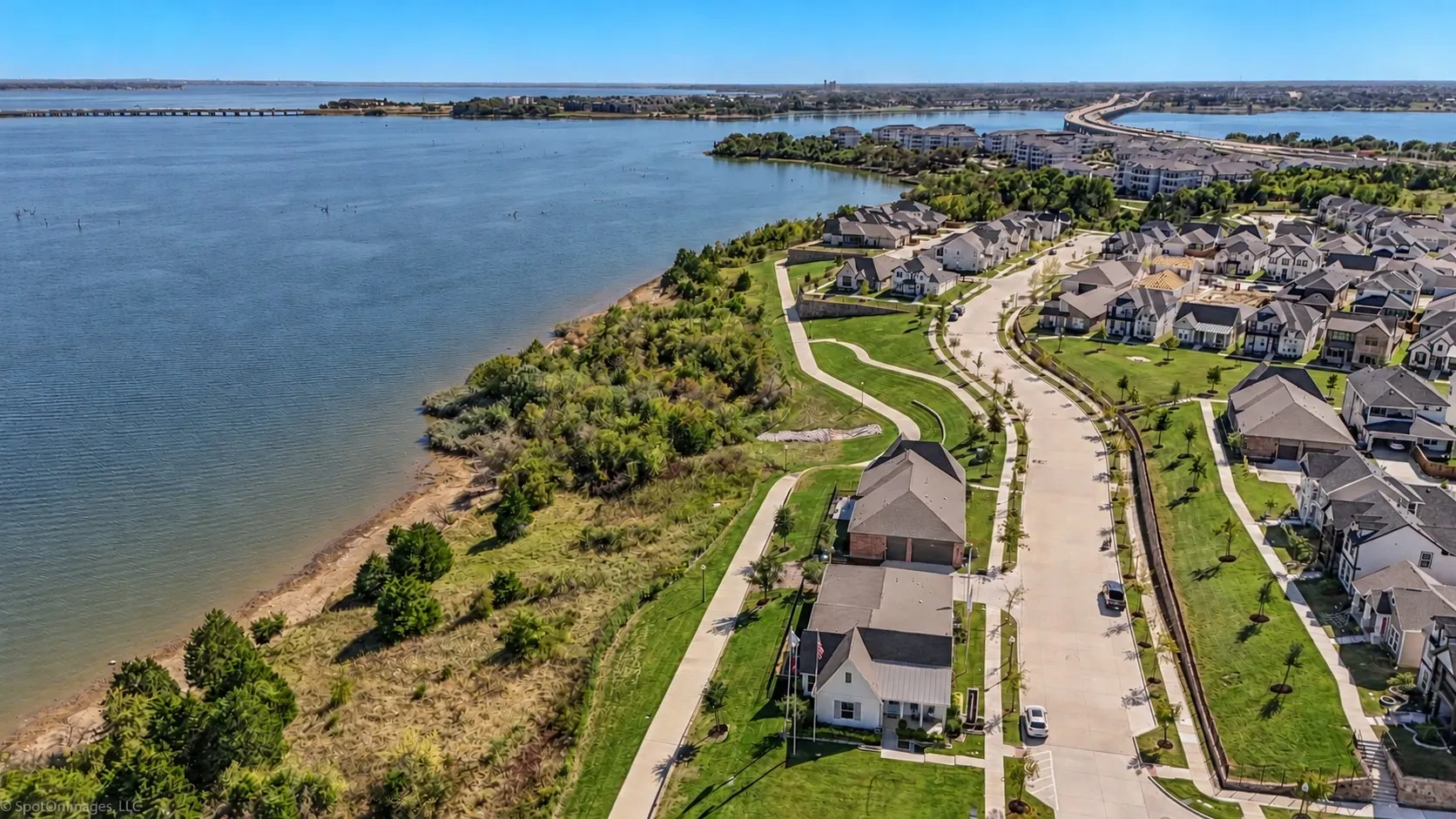 Aerial perspective of a developed residential community featuring waterfront properties, a winding street, and manicured green spaces
