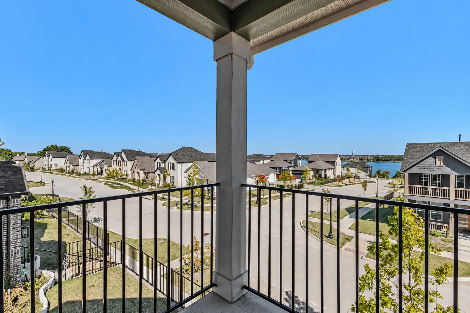 Balcony with a black metal railing and a concrete floor, offering neighborhood scenery and a distant body of water