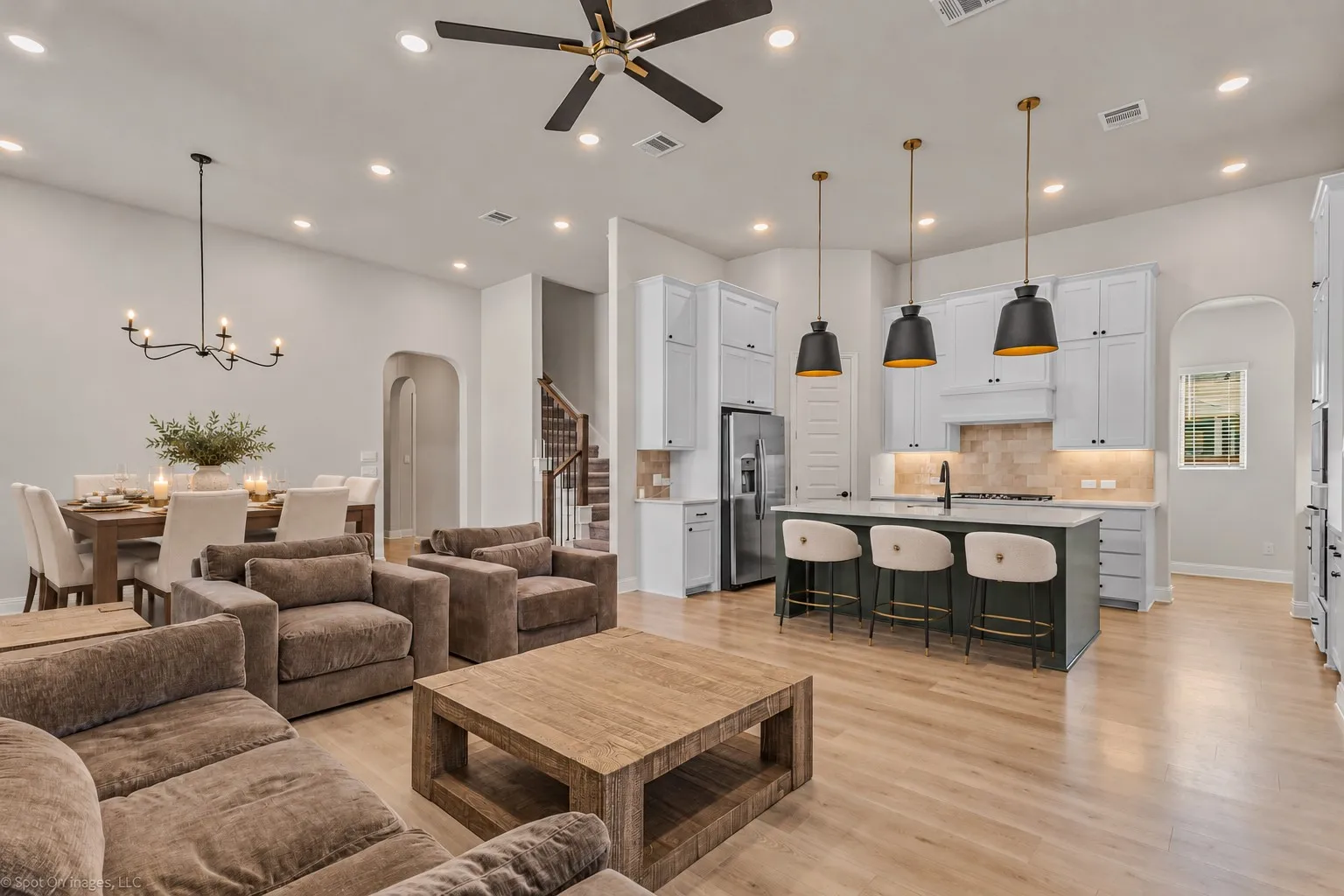 Open-concept living space featuring wood-finish flooring, a contemporary kitchen island with pendant lighting, white shaker cabinetry, and a dining area with a chandelier
