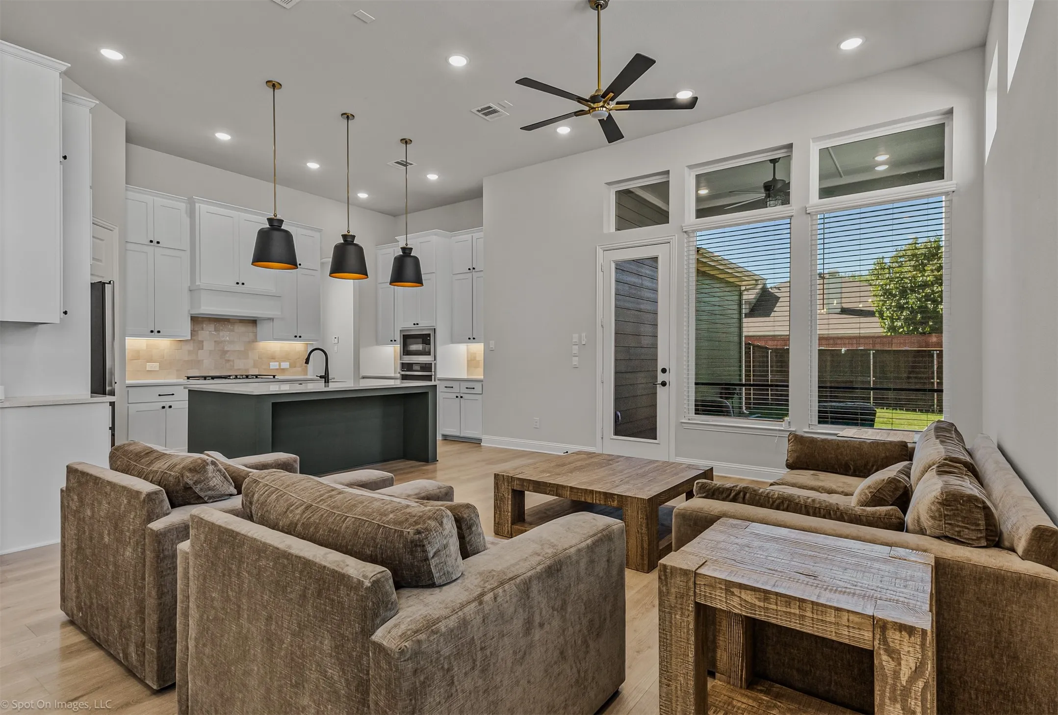 Open concept living area with light wood-finish flooring, recessed lighting, and a dark-toned kitchen island with a single basin sink