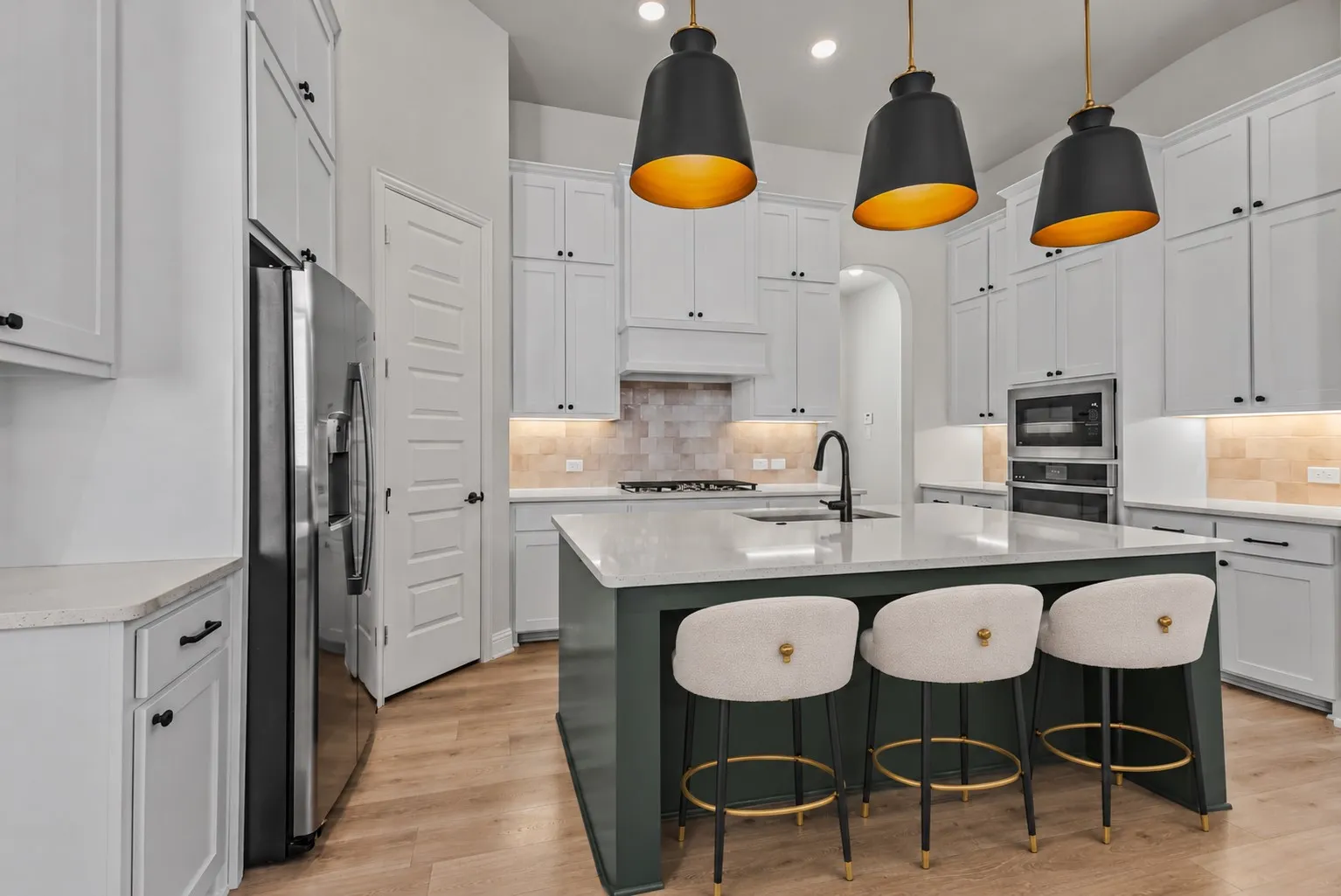 Kitchen featuring light wood-finish flooring, white cabinetry, integrated stainless steel appliances, a center island with a light-toned countertop, and recessed lighting