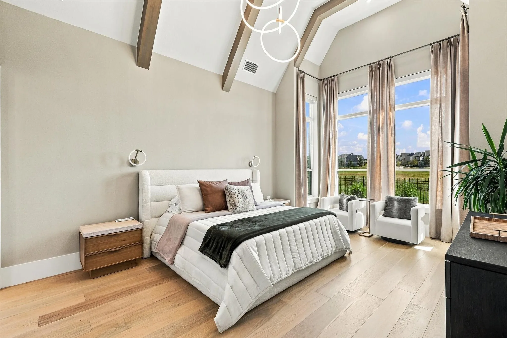 Vaulted ceiling with exposed wood beams, wood-finish flooring, three large windows, modern circular pendant lighting, and wall-mounted sconces