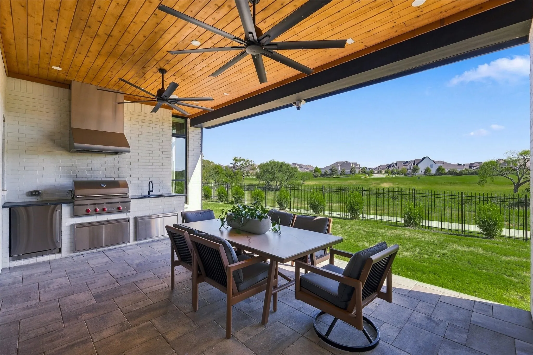Covered outdoor living space featuring an outdoor kitchen with built-in grill, stainless steel appliances, a wood-paneled ceiling, and large ceiling fans