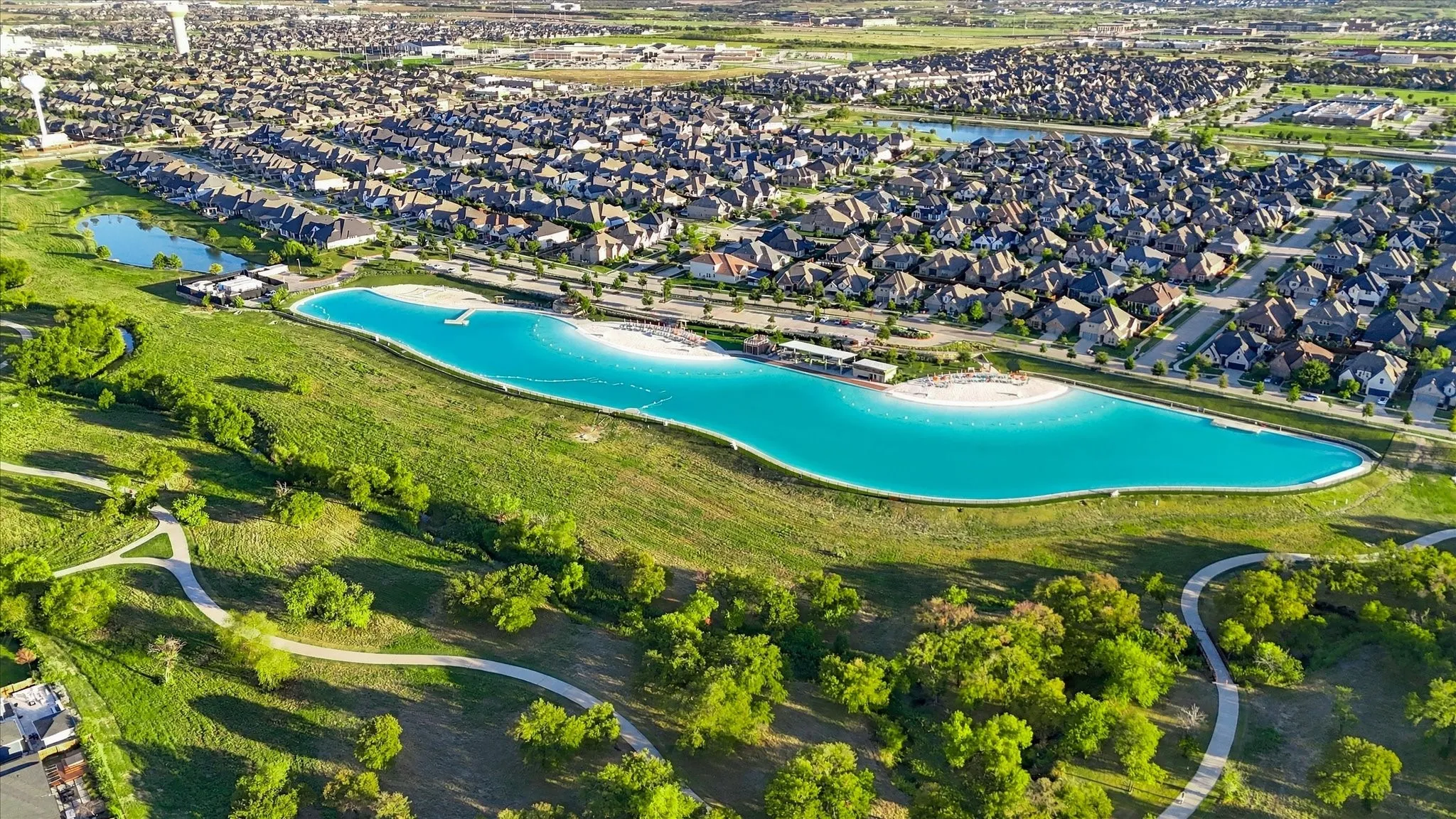 Expansive residential development featuring a large lagoon with a white sand beach, paved walking paths, and abundant green spaces