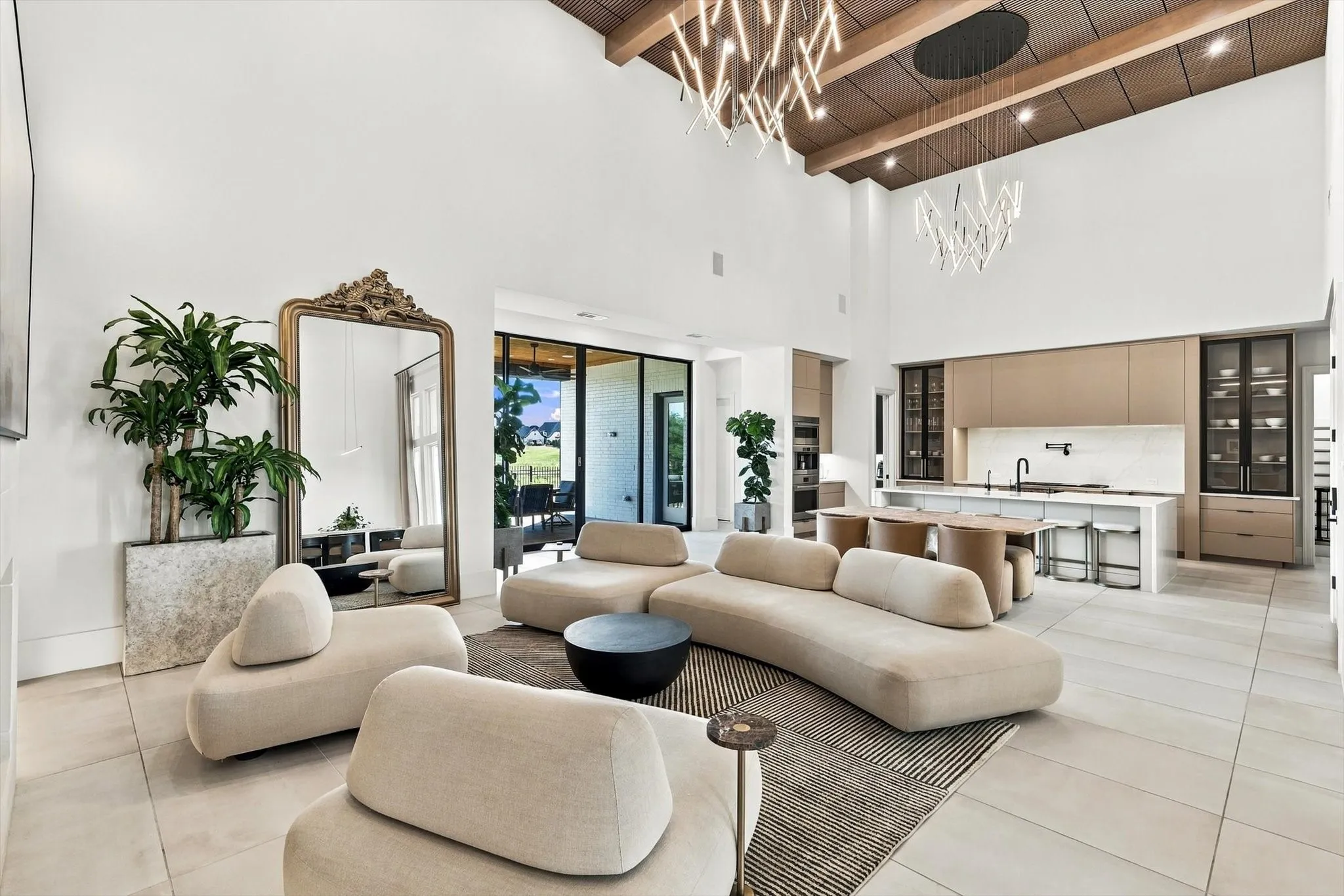 Two-story ceiling with exposed wood beams, modern overhead lighting, recessed lighting, expansive glass sliding doors, and a kitchen featuring a large island with seating