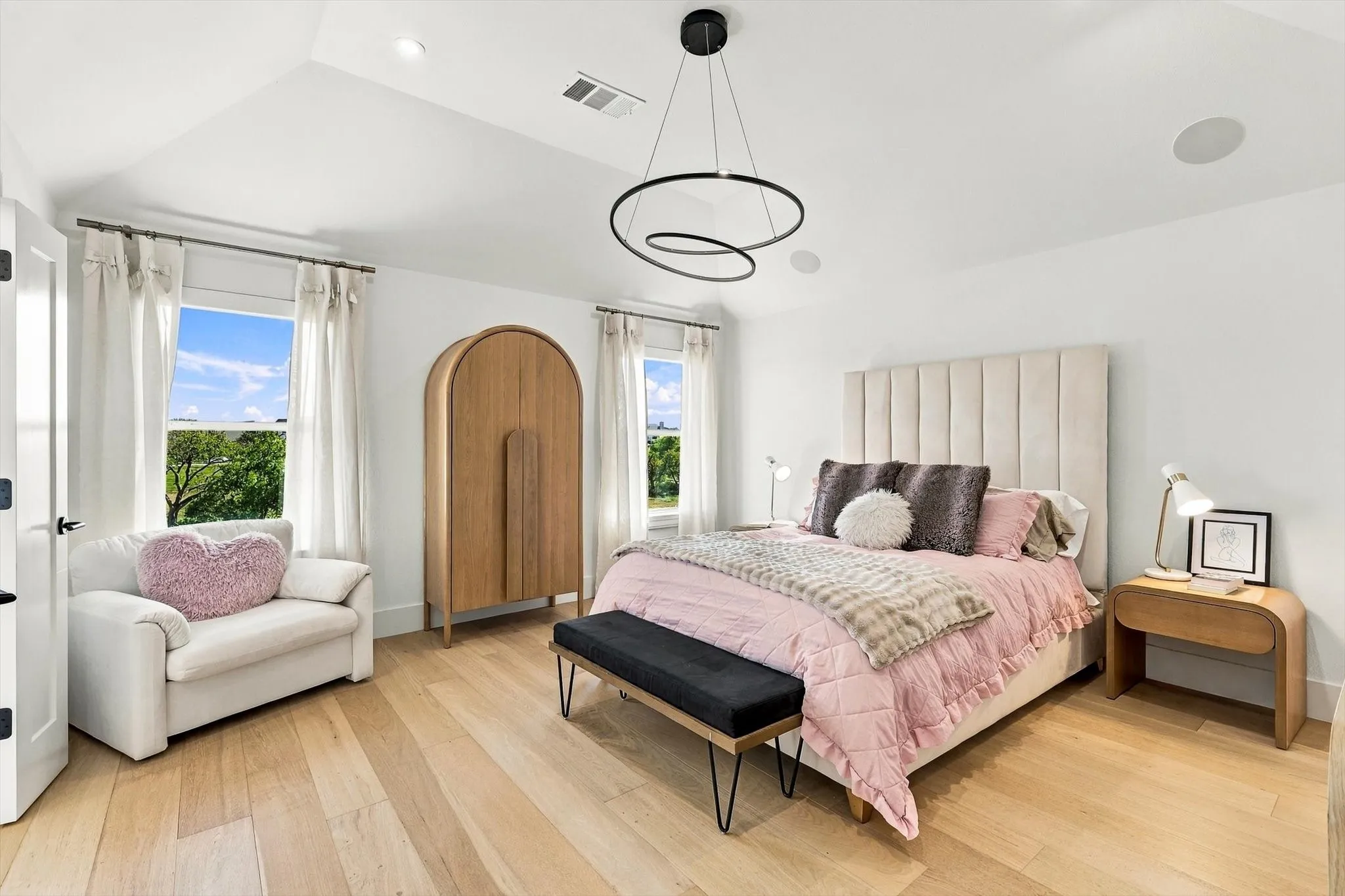 Vaulted ceiling, light wood-finish flooring, two windows with white trim, built-in ceiling speakers, and a contemporary circular chandelier