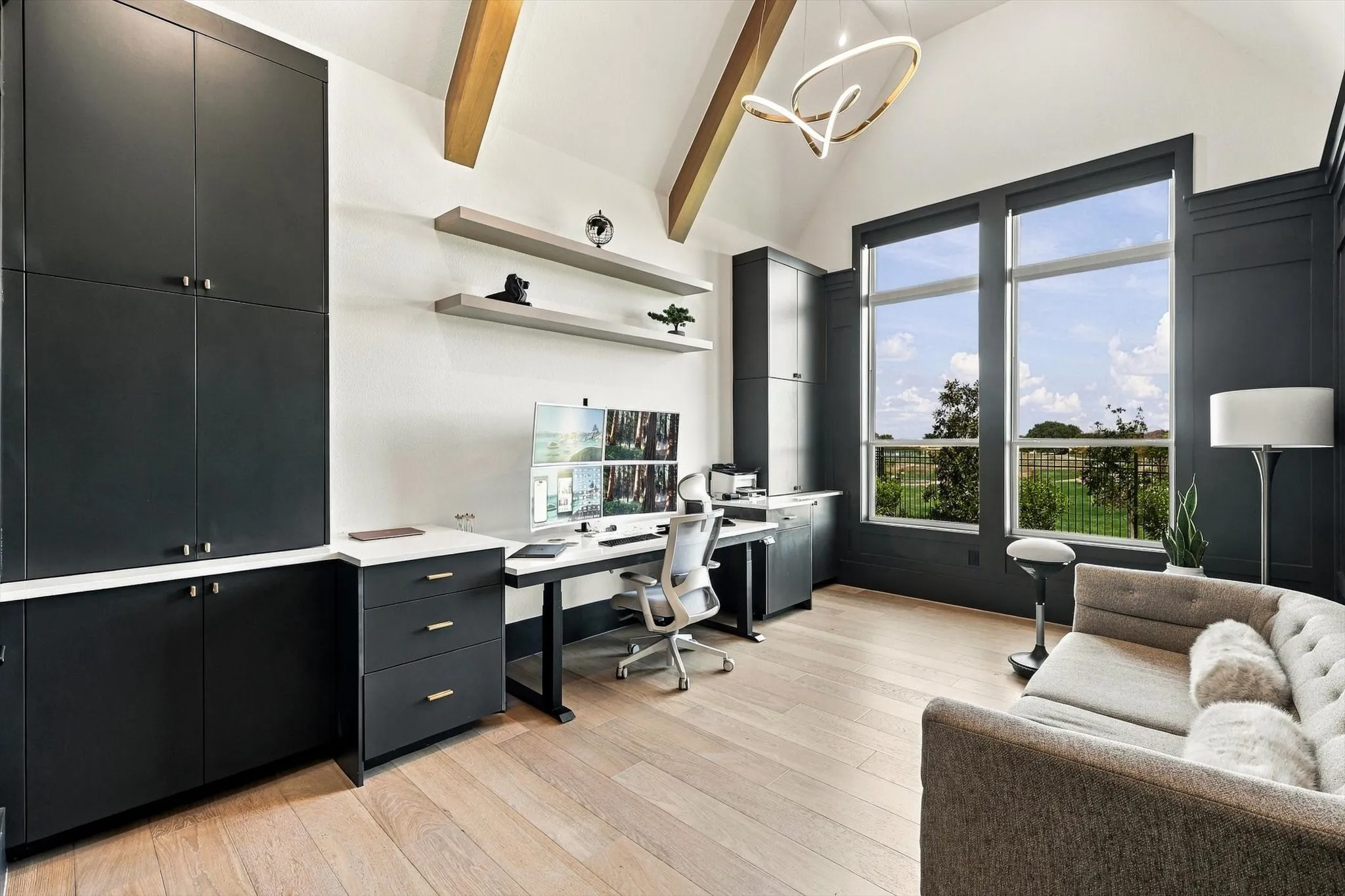 Vaulted ceiling with exposed wood beams, extensive built-in cabinetry with white countertops, large windows, wood-finish flooring, and a contemporary chandelier