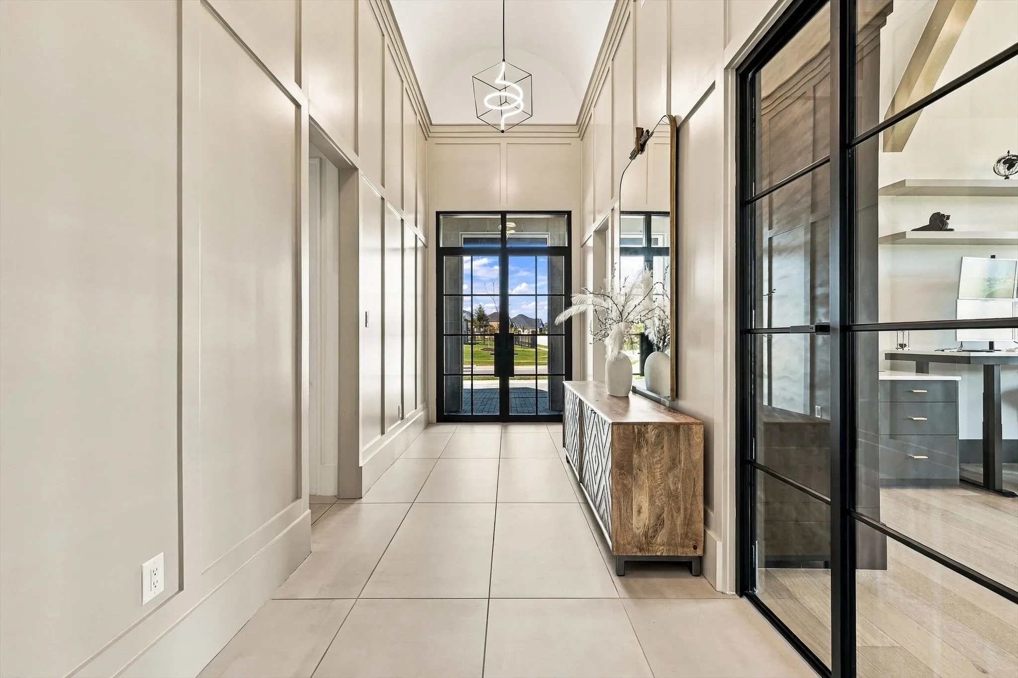 Board and batten wall detailing, arched ceiling, contemporary chandelier, black-framed glass entry door, and large format tile flooring