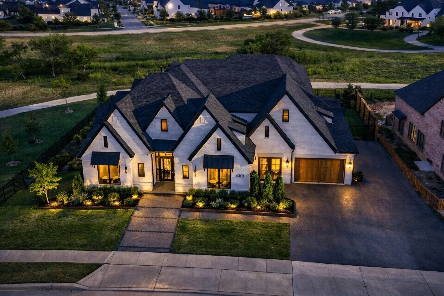 White stucco exterior with dark-pitched roofs, a wood-finish garage door, and a paver walkway