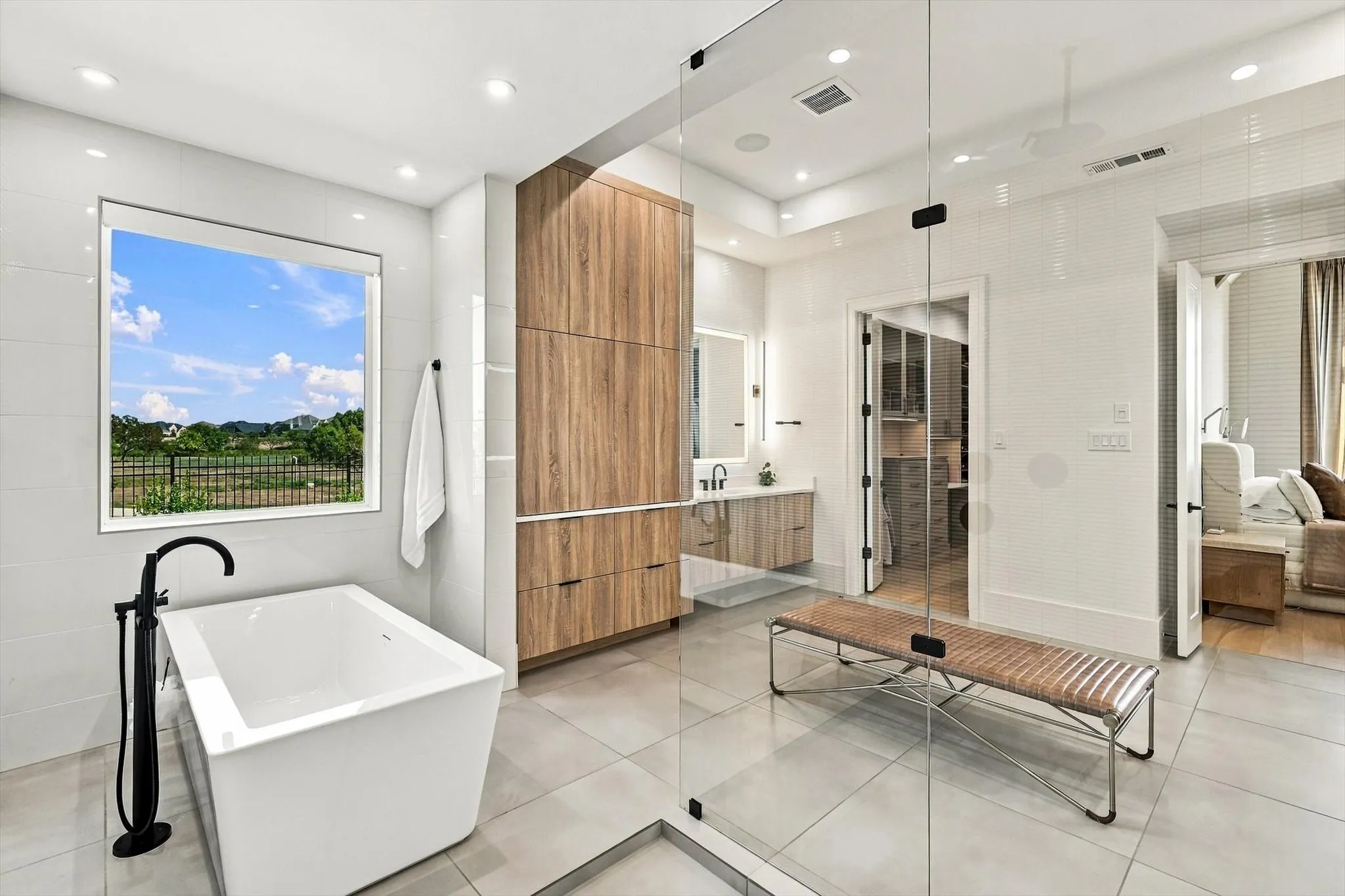 Freestanding soaking tub with a matte black floor-mounted faucet, a wood-finish vanity with an undermount sink, and a glass-enclosed shower