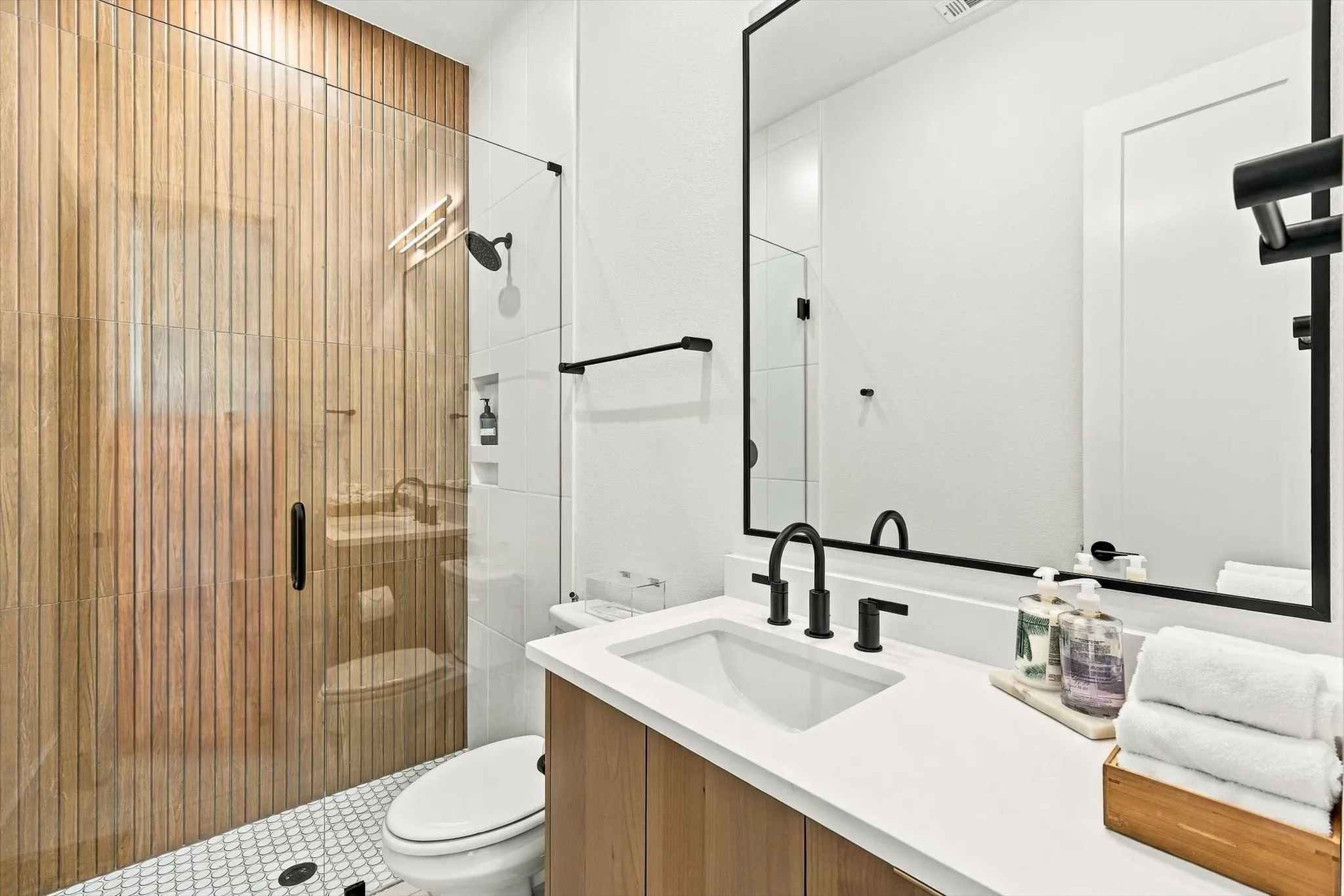 Walk-in shower with wood-finish tile surround, glass enclosure, and recessed shelving