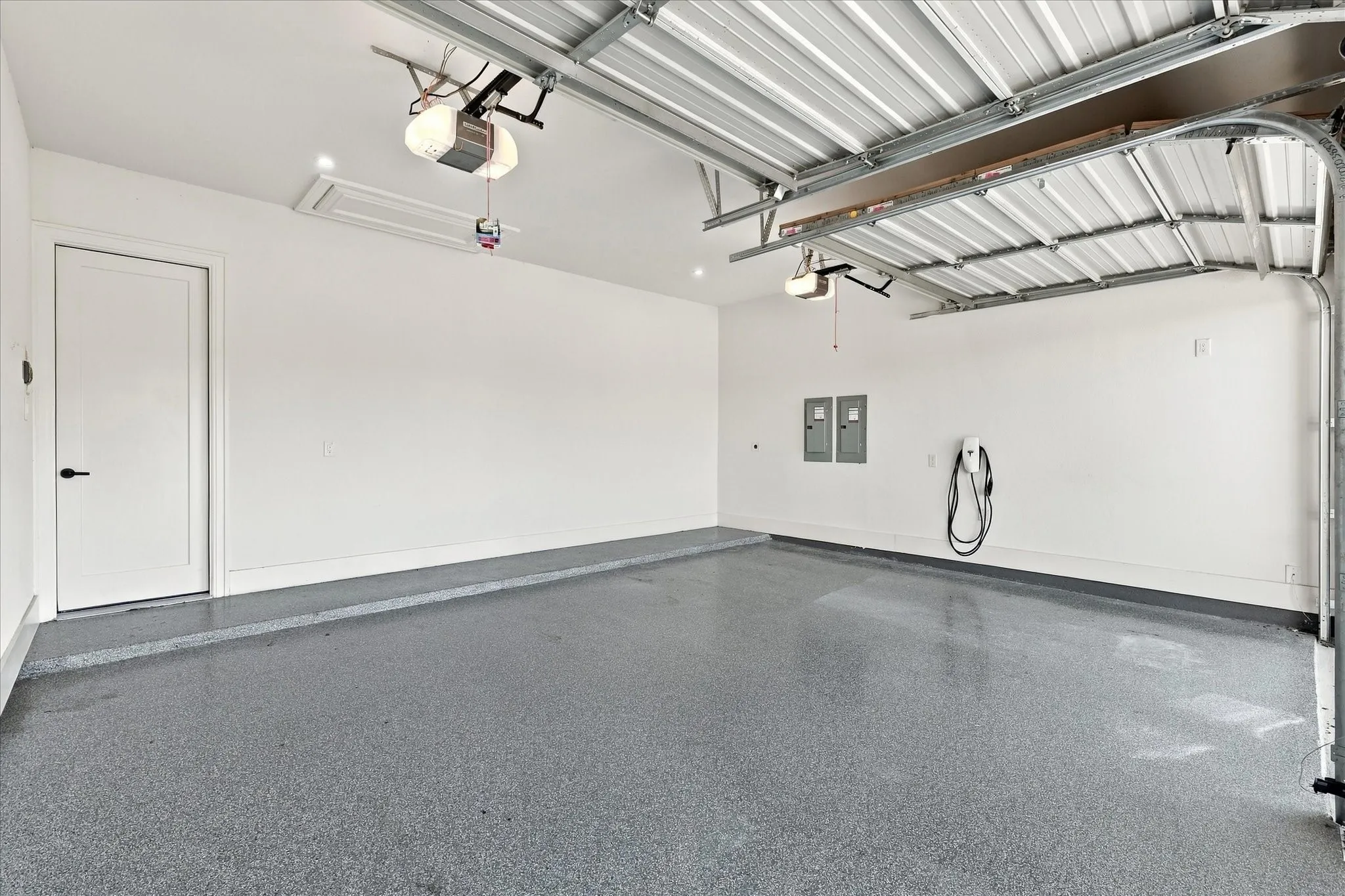 Spacious garage featuring a durable epoxy floor, integrated overhead lighting, and an electric vehicle charging station
