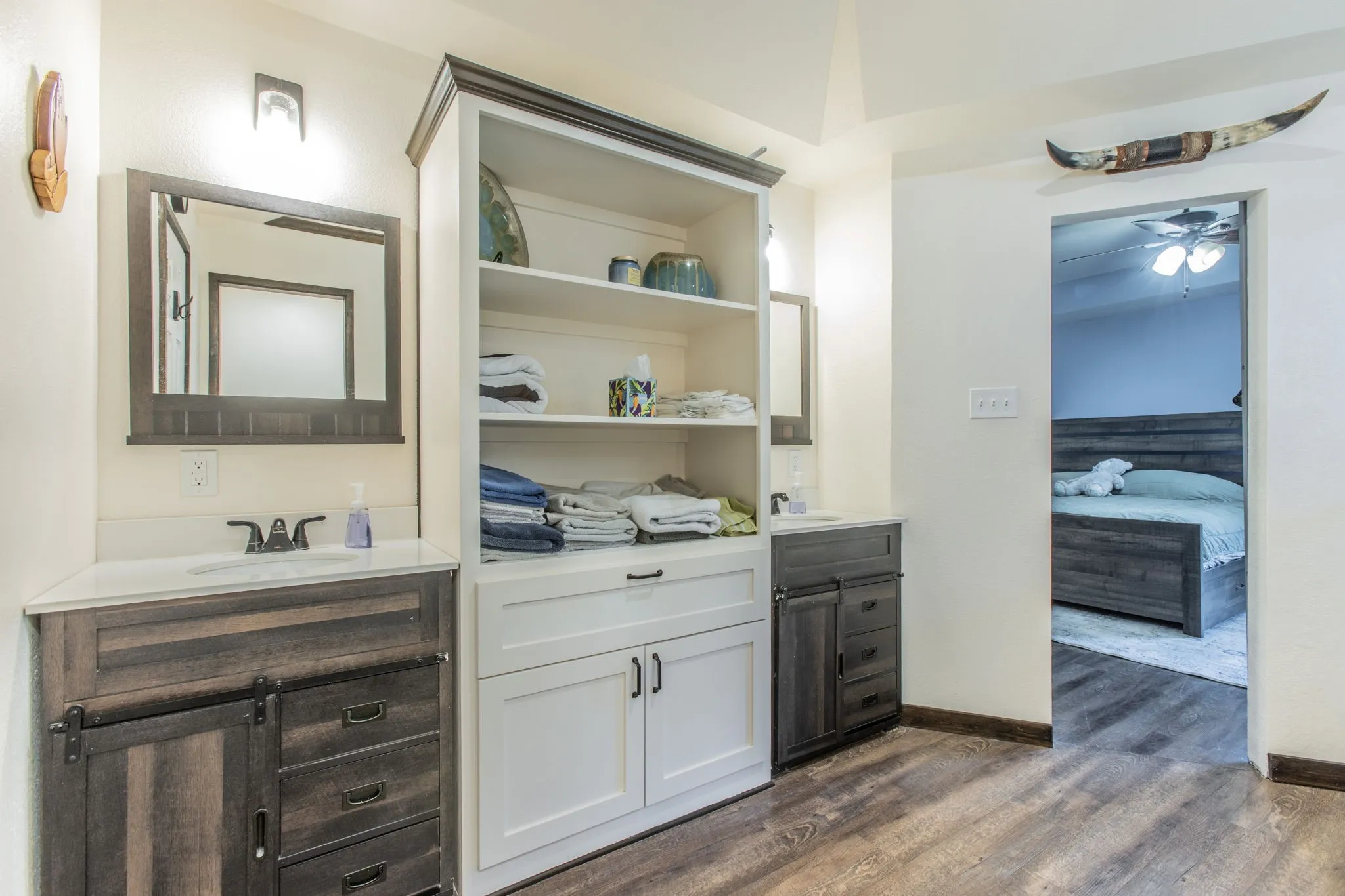 Dual wood-finish vanities with undermount sinks, built-in shelving, white countertops, and wood-finish flooring