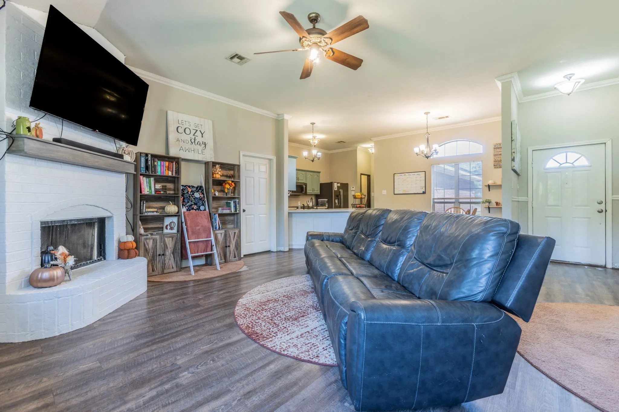Wood-finish flooring throughout, white brick fireplace with hearth, ceiling fan with integrated lighting, recessed lighting, and a front entry door with an arched window