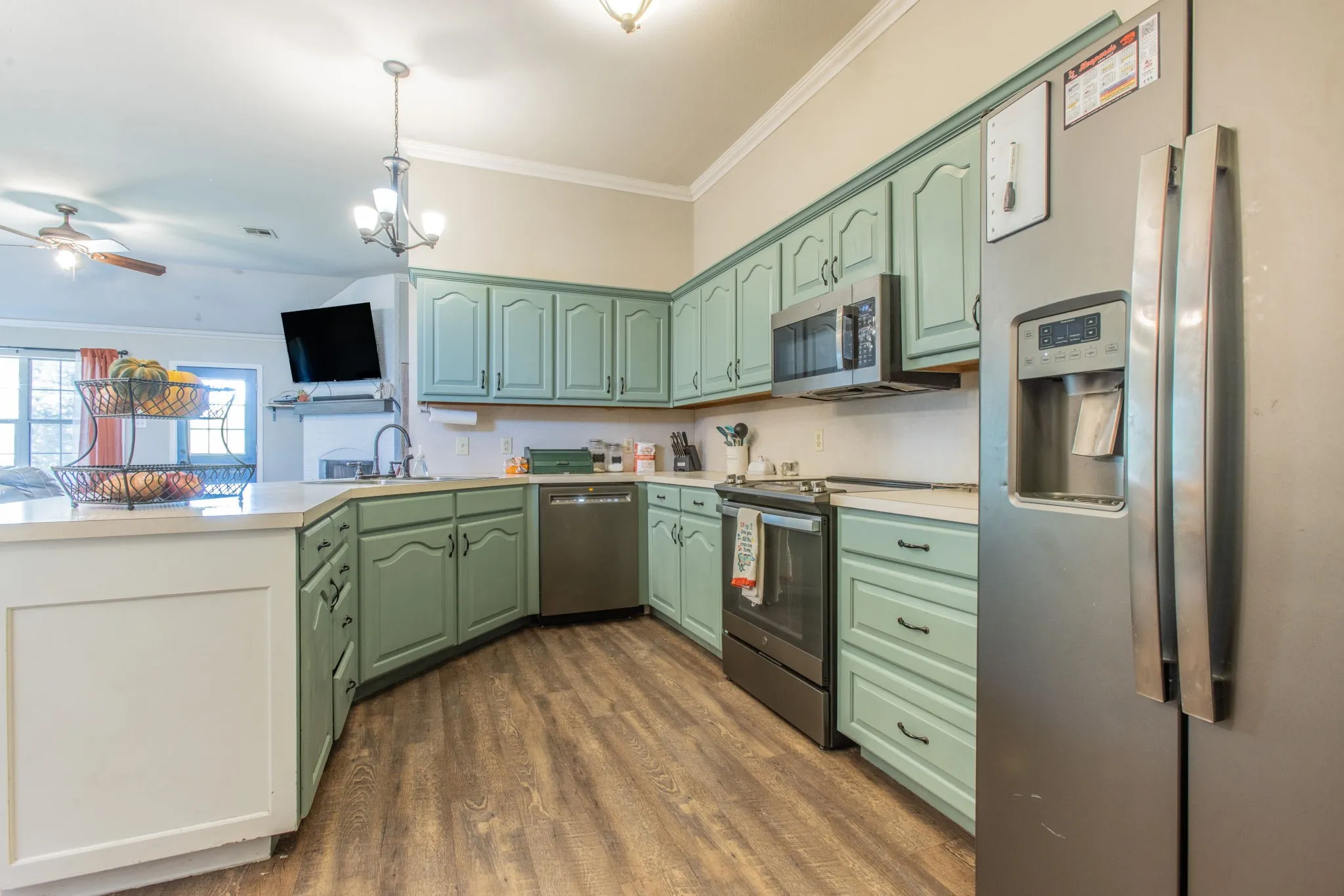 Kitchen with wood-finish flooring, light green cabinetry, stainless steel appliances, and solid surface countertops