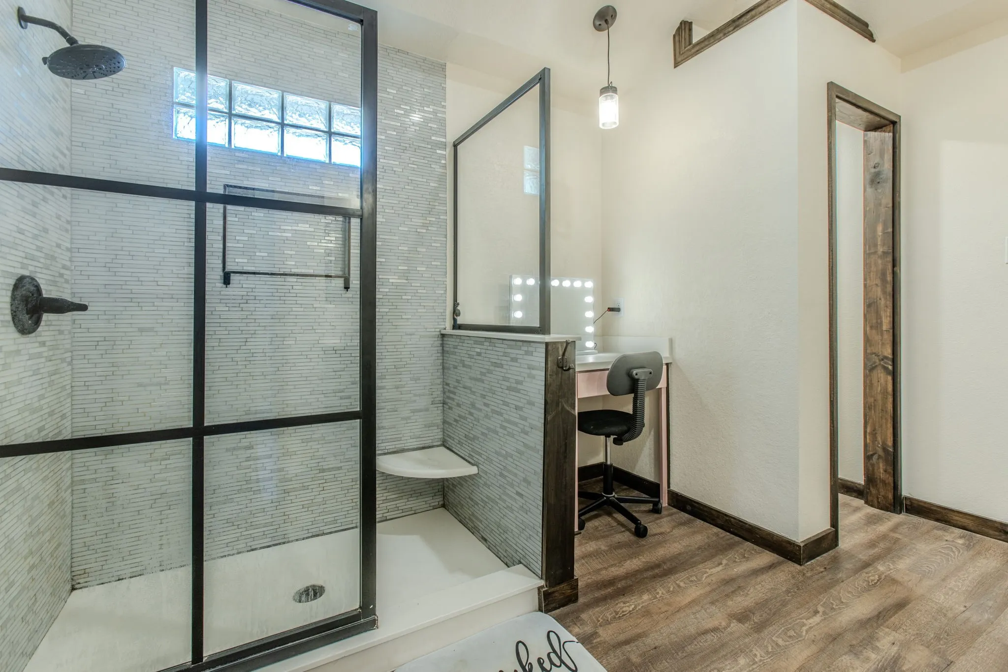 Walk-in shower with dark-framed glass enclosure, built-in corner bench, and mosaic tile surround