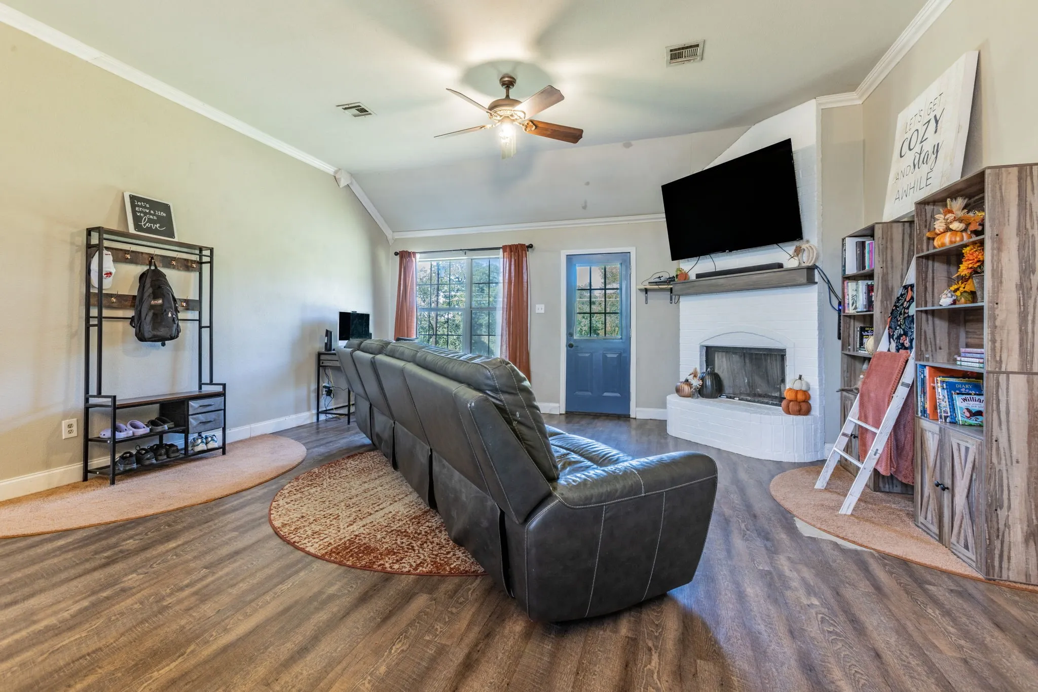 Vaulted ceiling with a ceiling fan, wood-finish flooring, white painted fireplace with a mantel, and a blue painted door with window panes