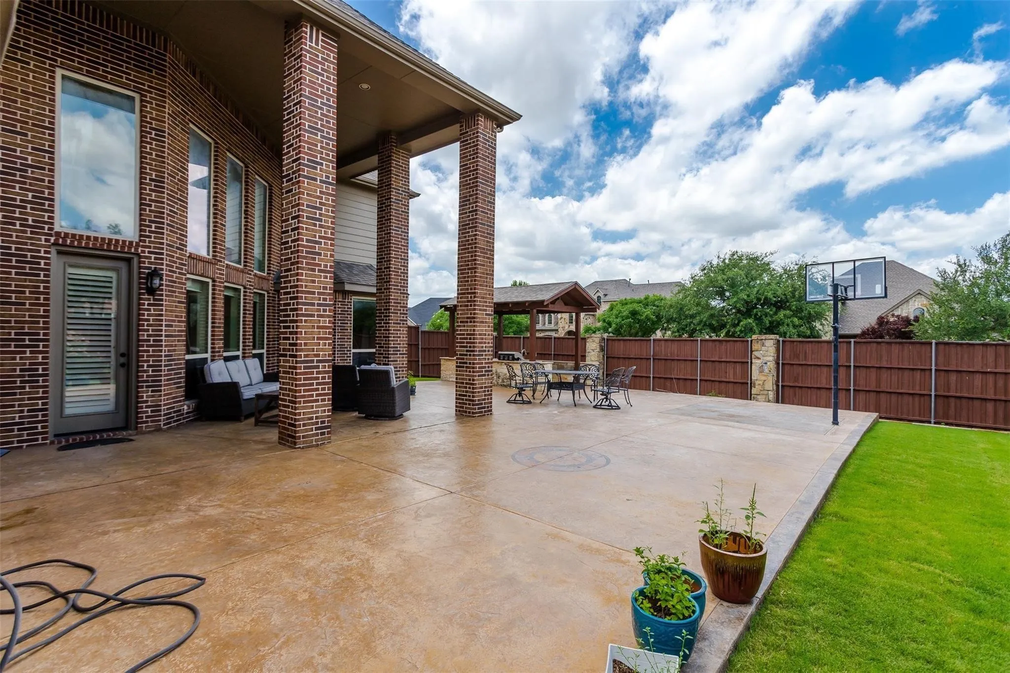 Expansive concrete patio with a covered outdoor area, brick columns, and a basketball hoop