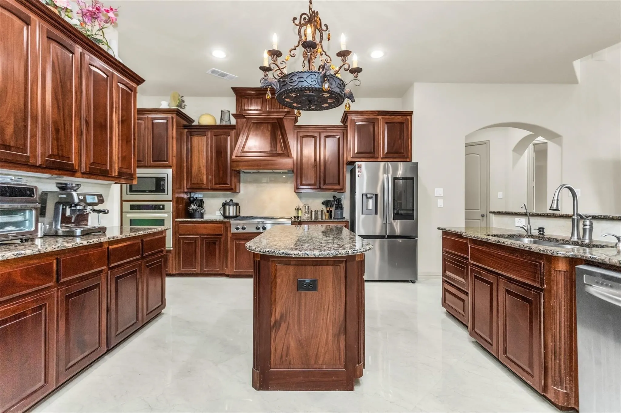 Expansive kitchen with wood cabinetry, granite countertops, stainless steel appliances, a kitchen island, and archway details
