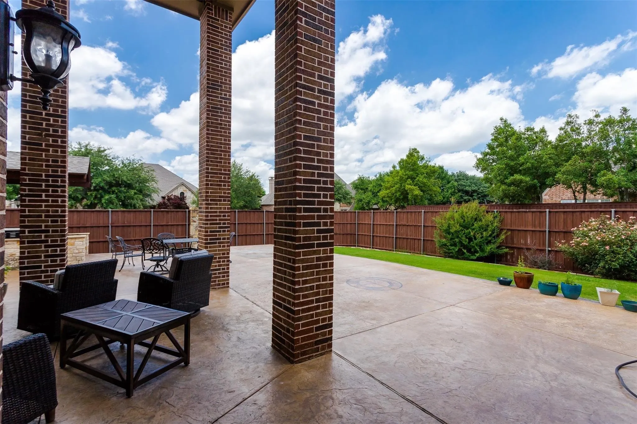 Covered patio featuring brick columns, stamped concrete flooring, and a manicured lawn area with a wood privacy fence