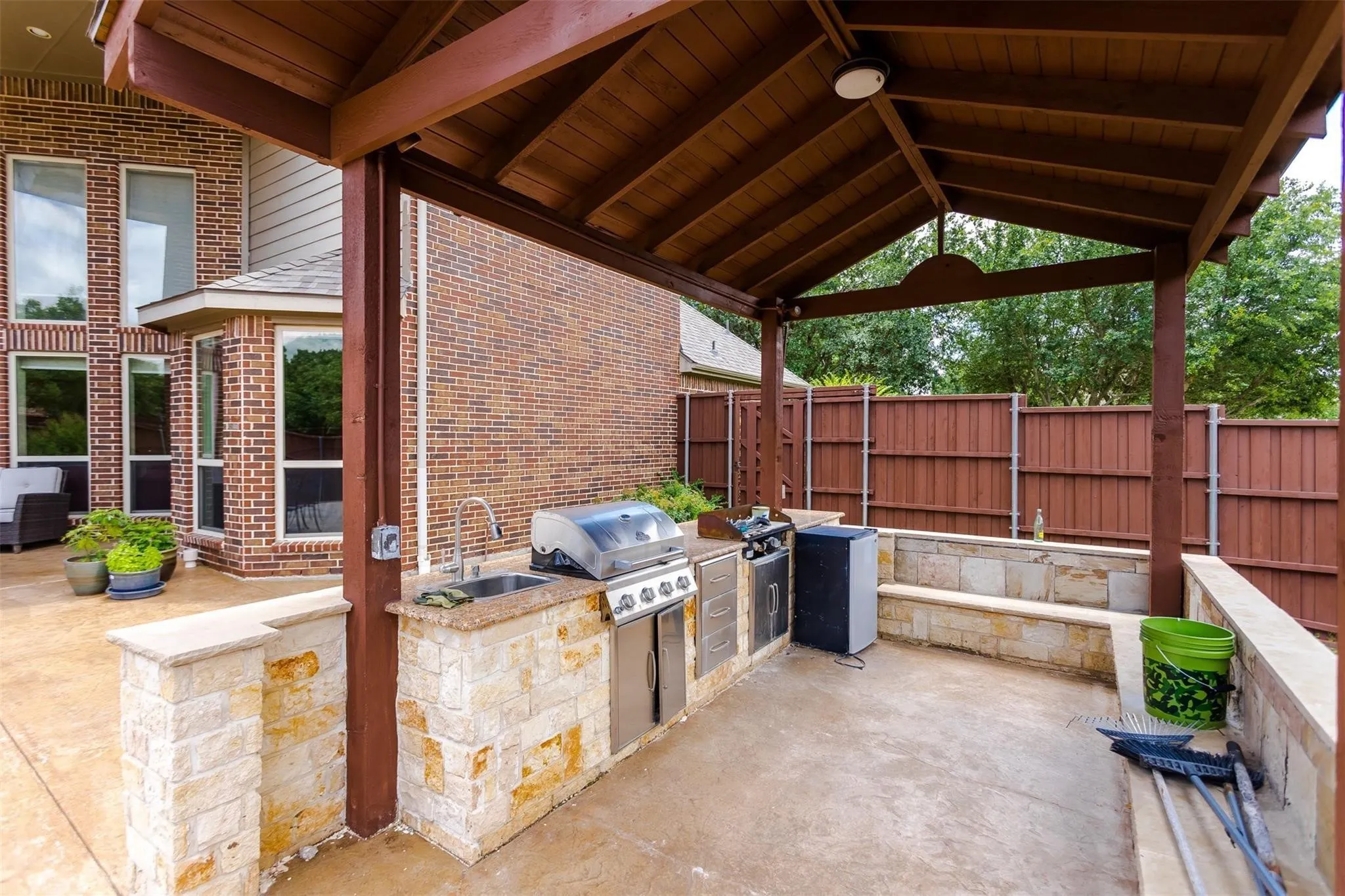 Covered outdoor kitchen featuring a built-in grill, sink, and stone-clad cabinetry