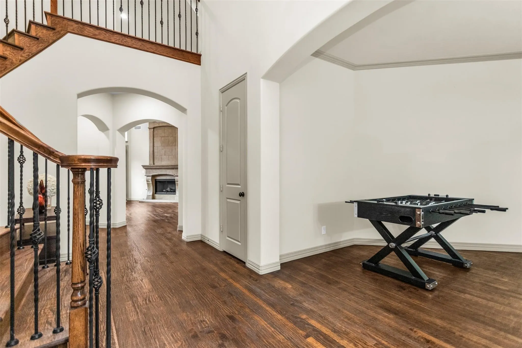 Hardwood flooring throughout, arched doorways, wrought iron stair balusters, and a stone-clad fireplace
