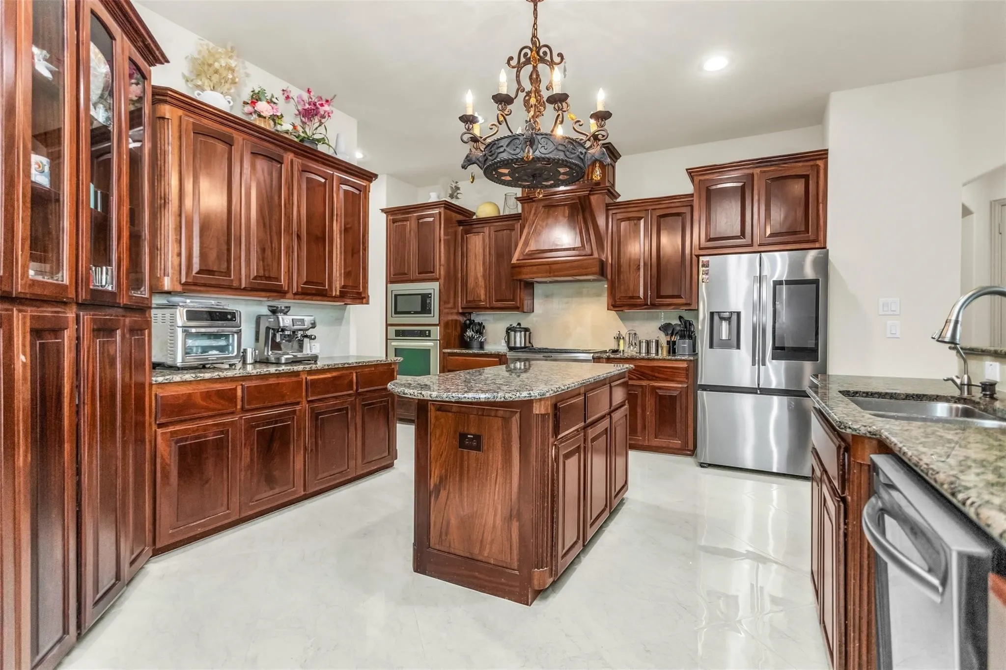 Kitchen featuring extensive wood cabinetry, granite countertops, stainless steel appliances, a center island, and a decorative chandelier