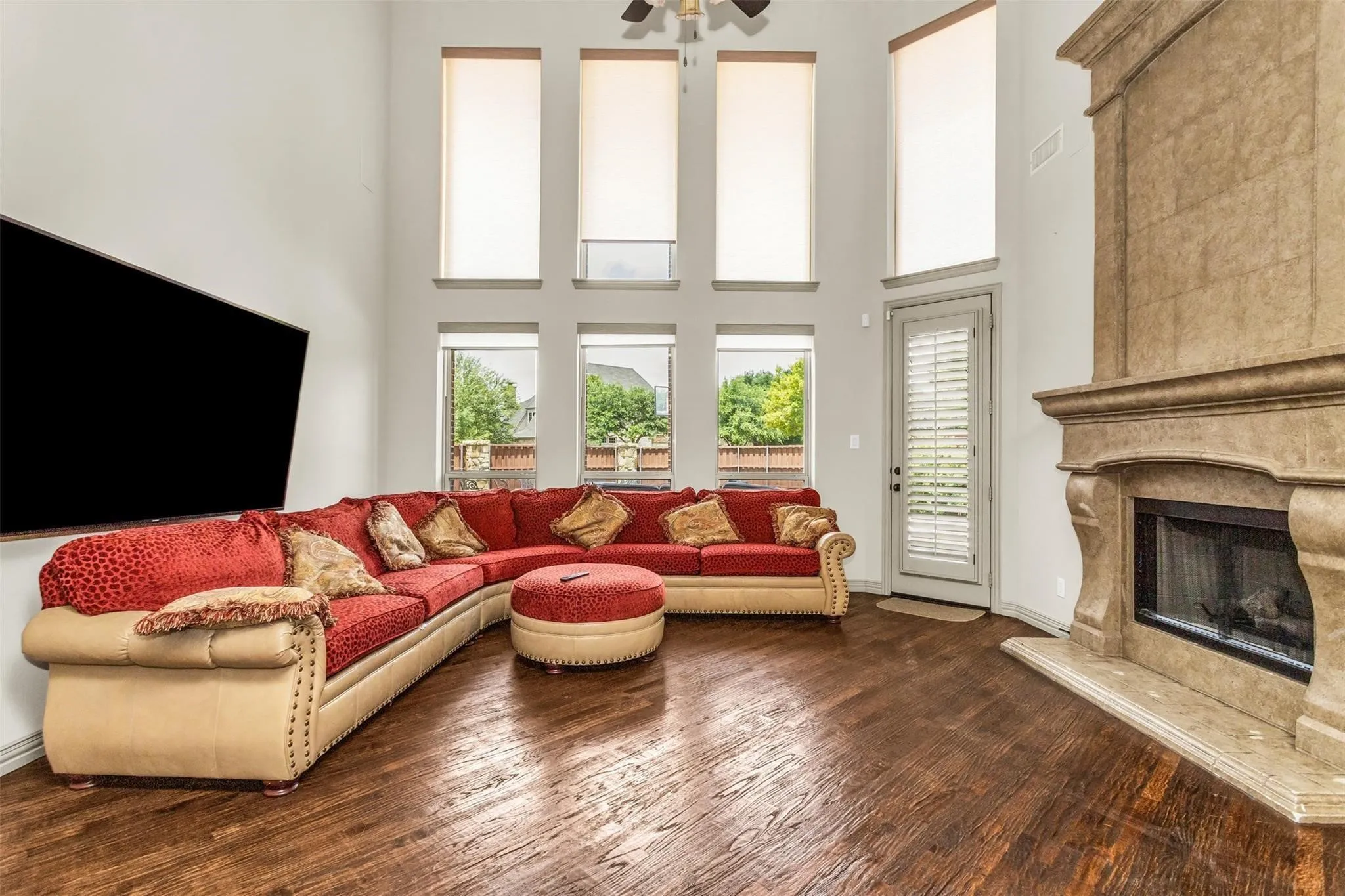 Two-story living area featuring wood-finish flooring, a stone-clad fireplace, and multiple windows with roller shades