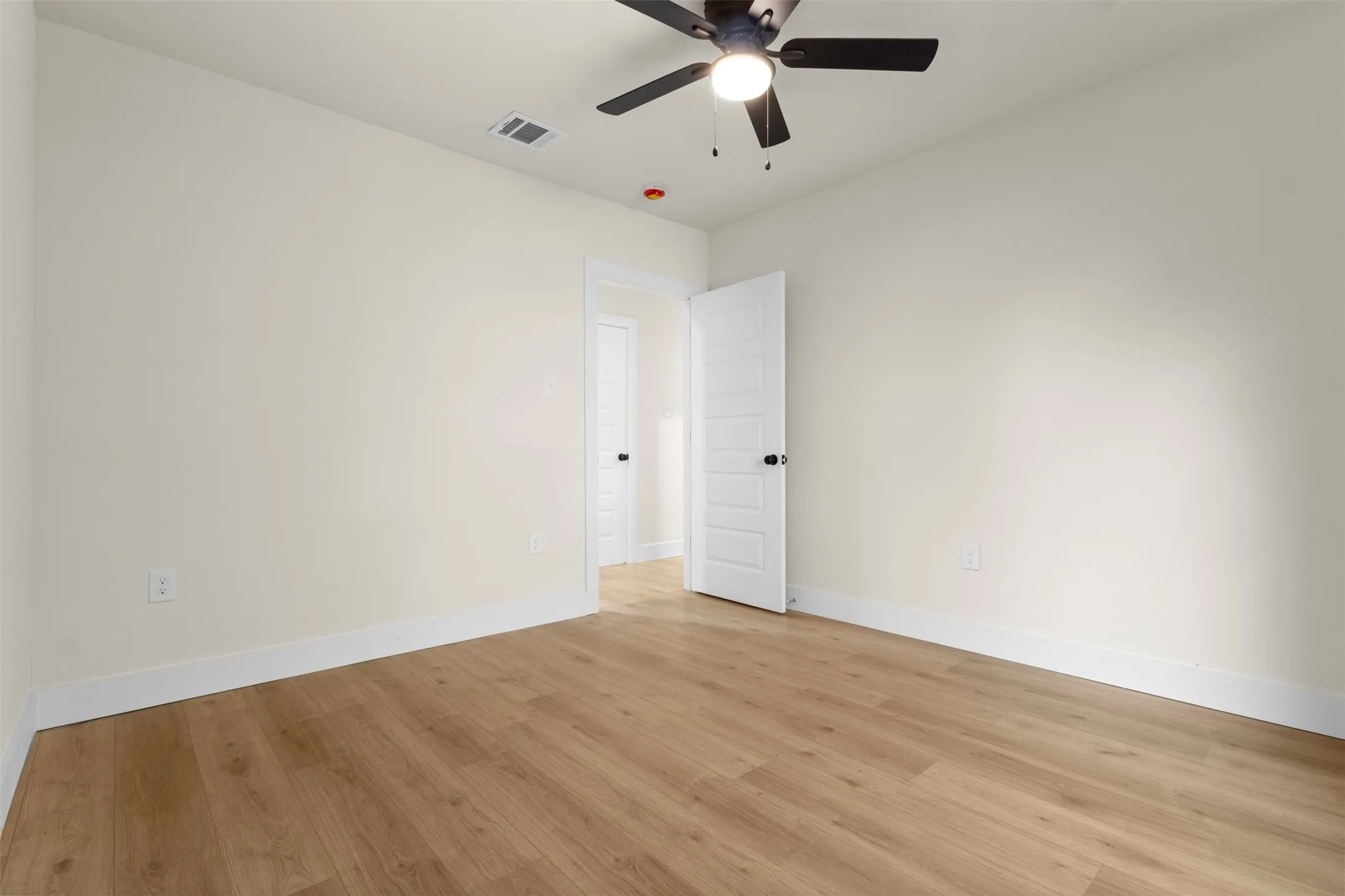 Wood-finish flooring with white baseboards, a ceiling fan with integrated lighting, and a paneled interior door