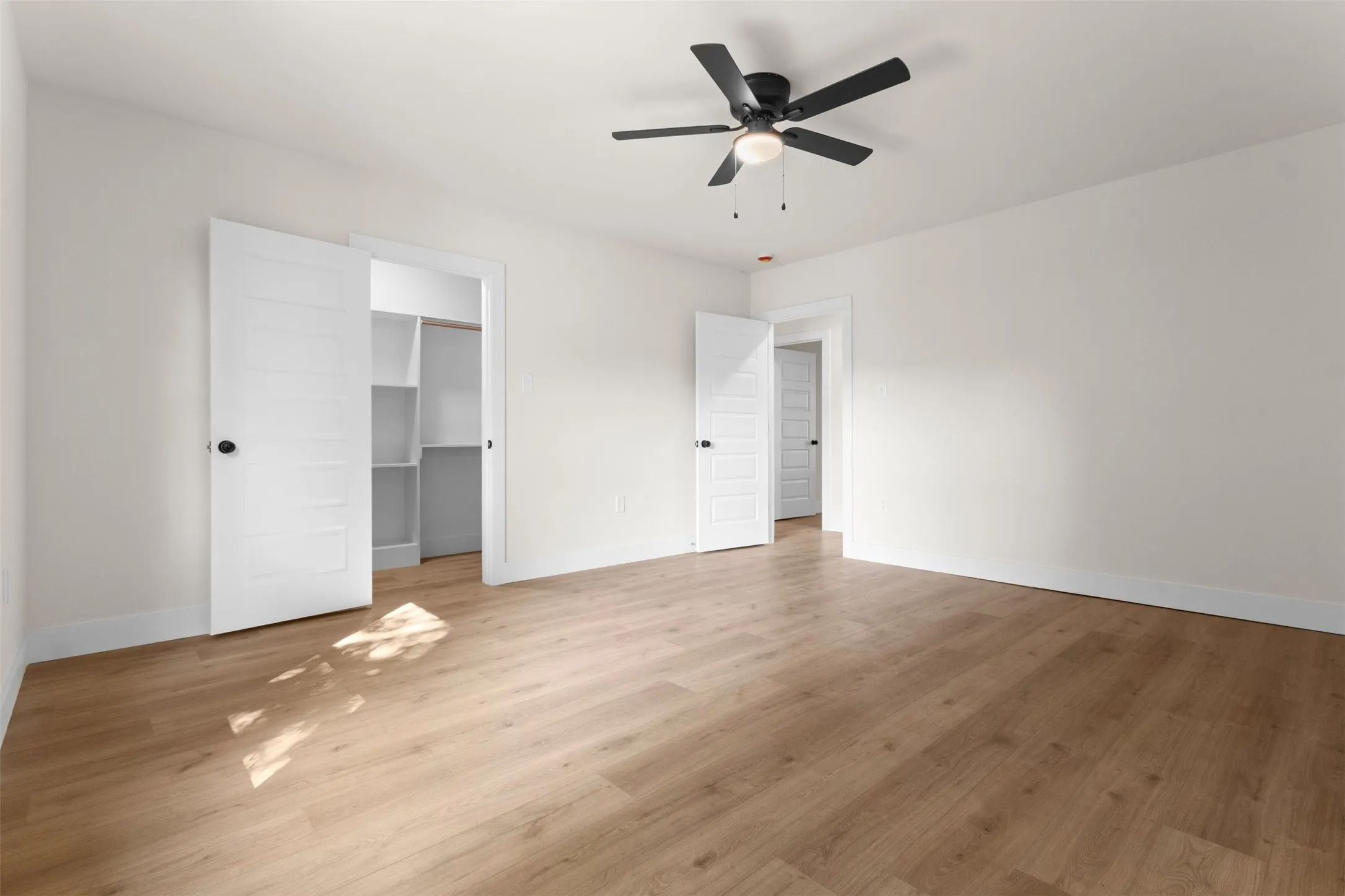 Recessed shelving, wood-finish flooring, white paneled doors, ceiling fan with integrated lighting, and neutral wall tones