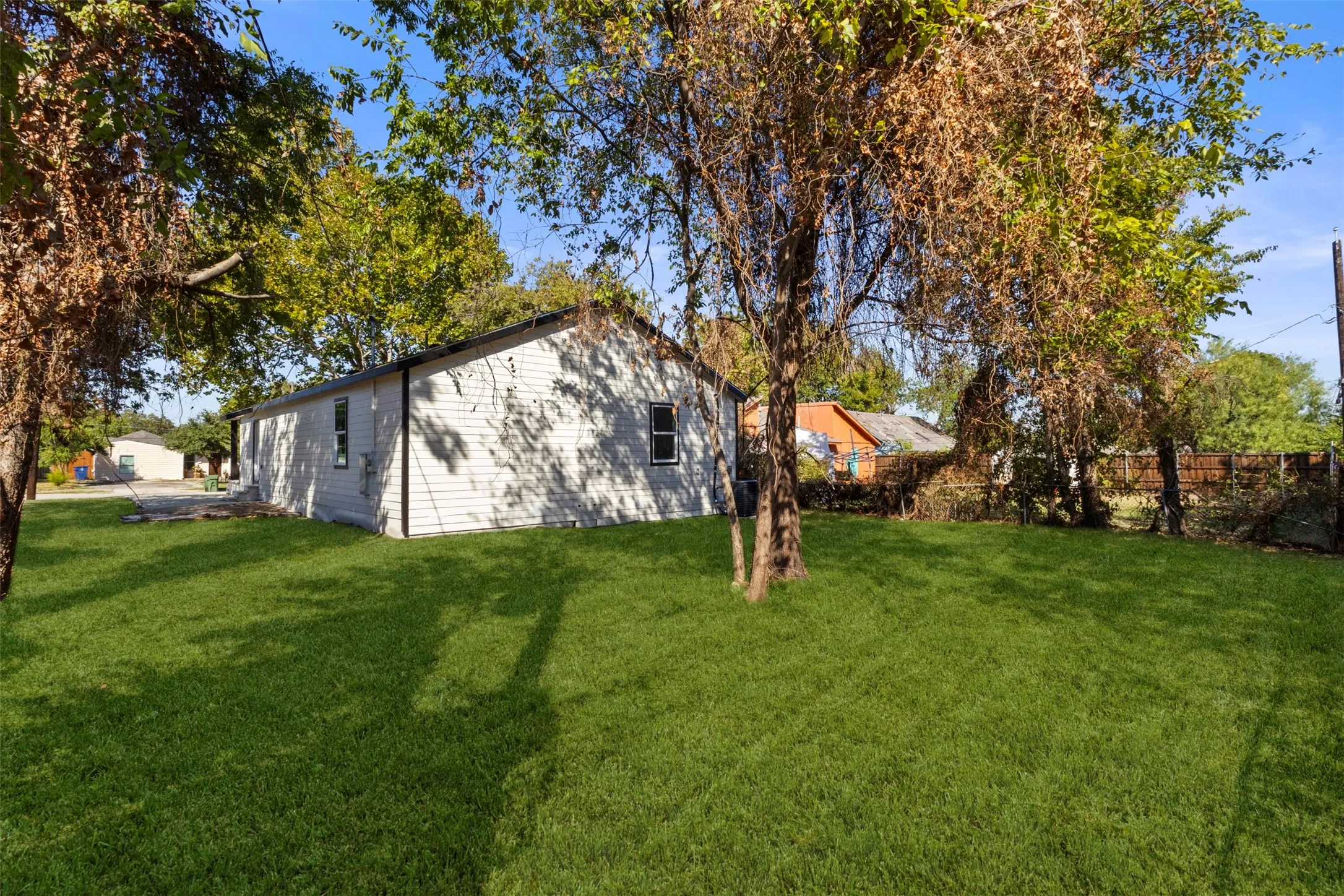Expansive grassy yard with mature trees and a white siding exterior
