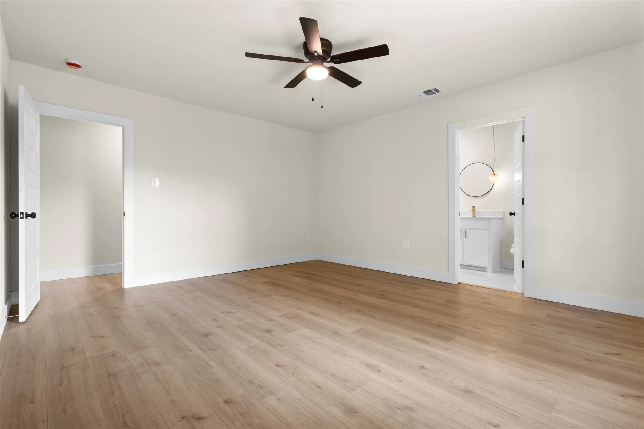 Spacious room featuring wood-finish flooring, light-colored walls, and a ceiling fan with integrated lighting