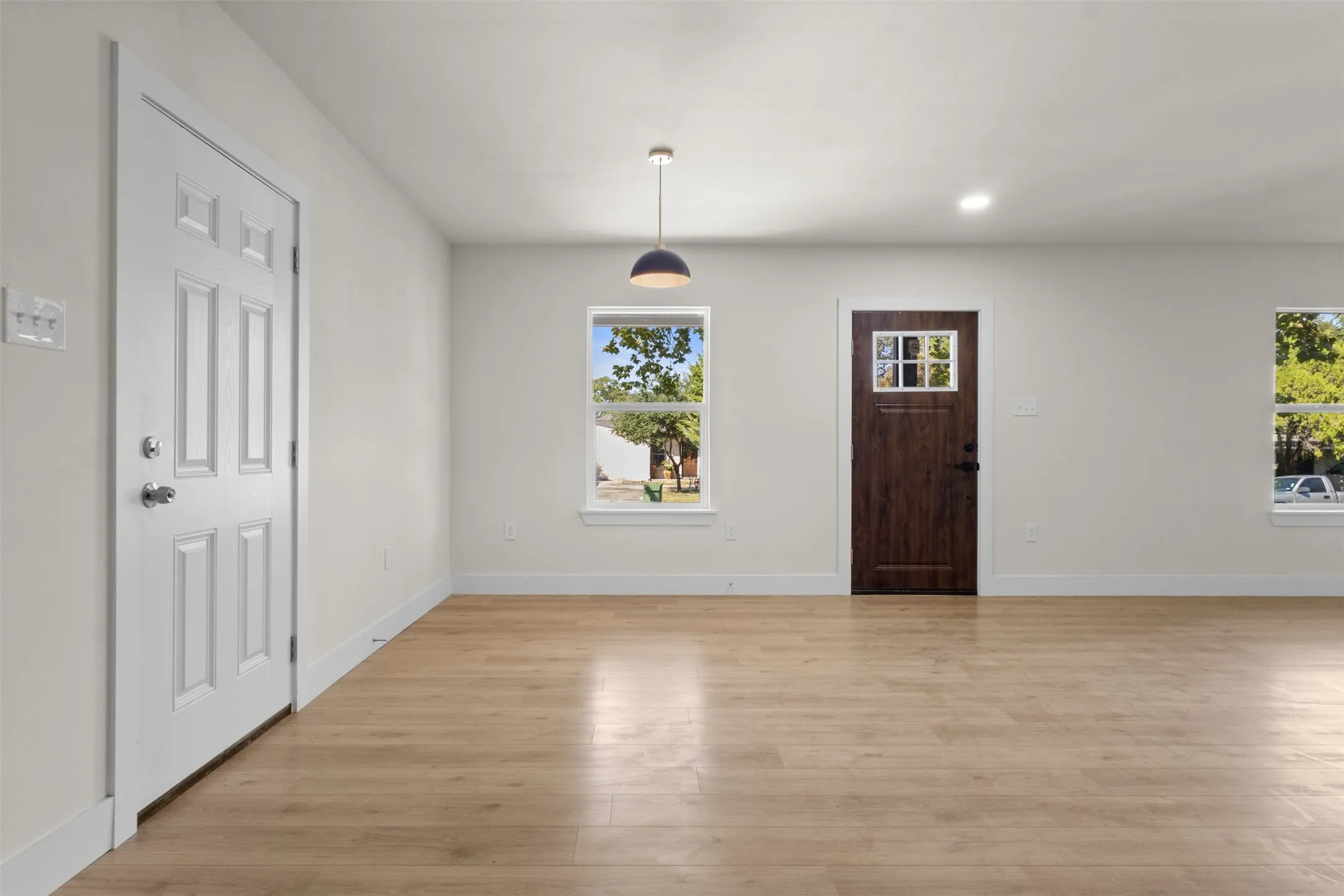 Wood-finish flooring, white walls, white trim, recessed lighting, and a modern pendant light