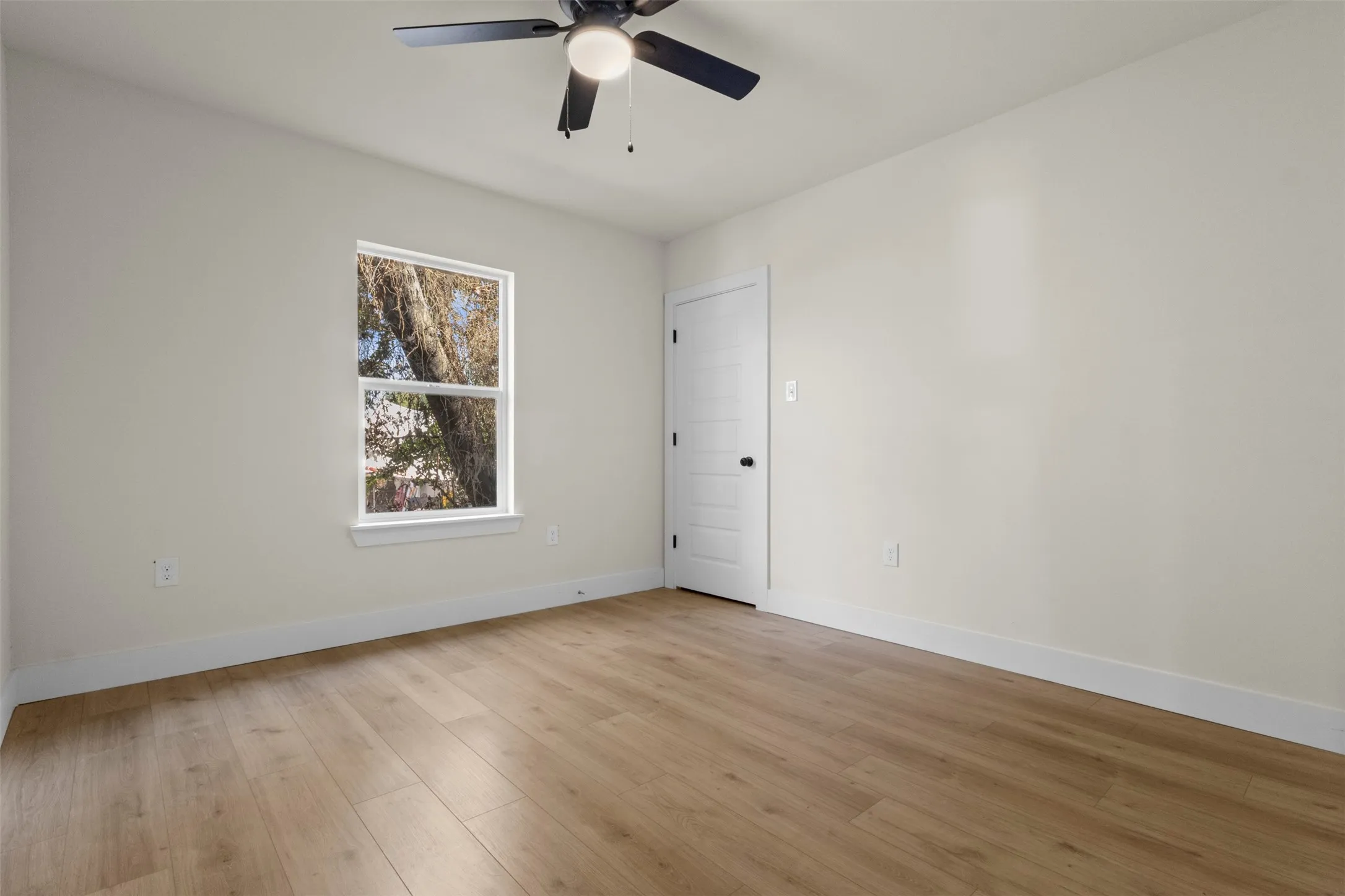 Neutral-toned walls with wood-finish flooring, a ceiling fan, and a white interior door