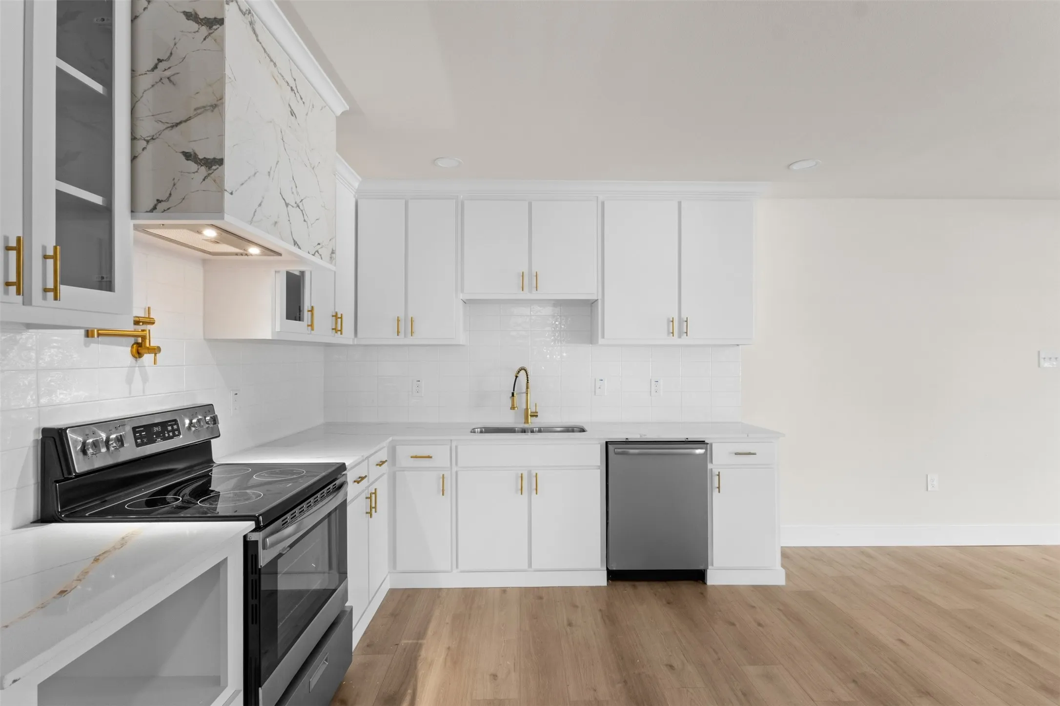 White cabinetry with gold-tone hardware, white subway tile backsplash, stainless steel appliances, and wood-finish flooring