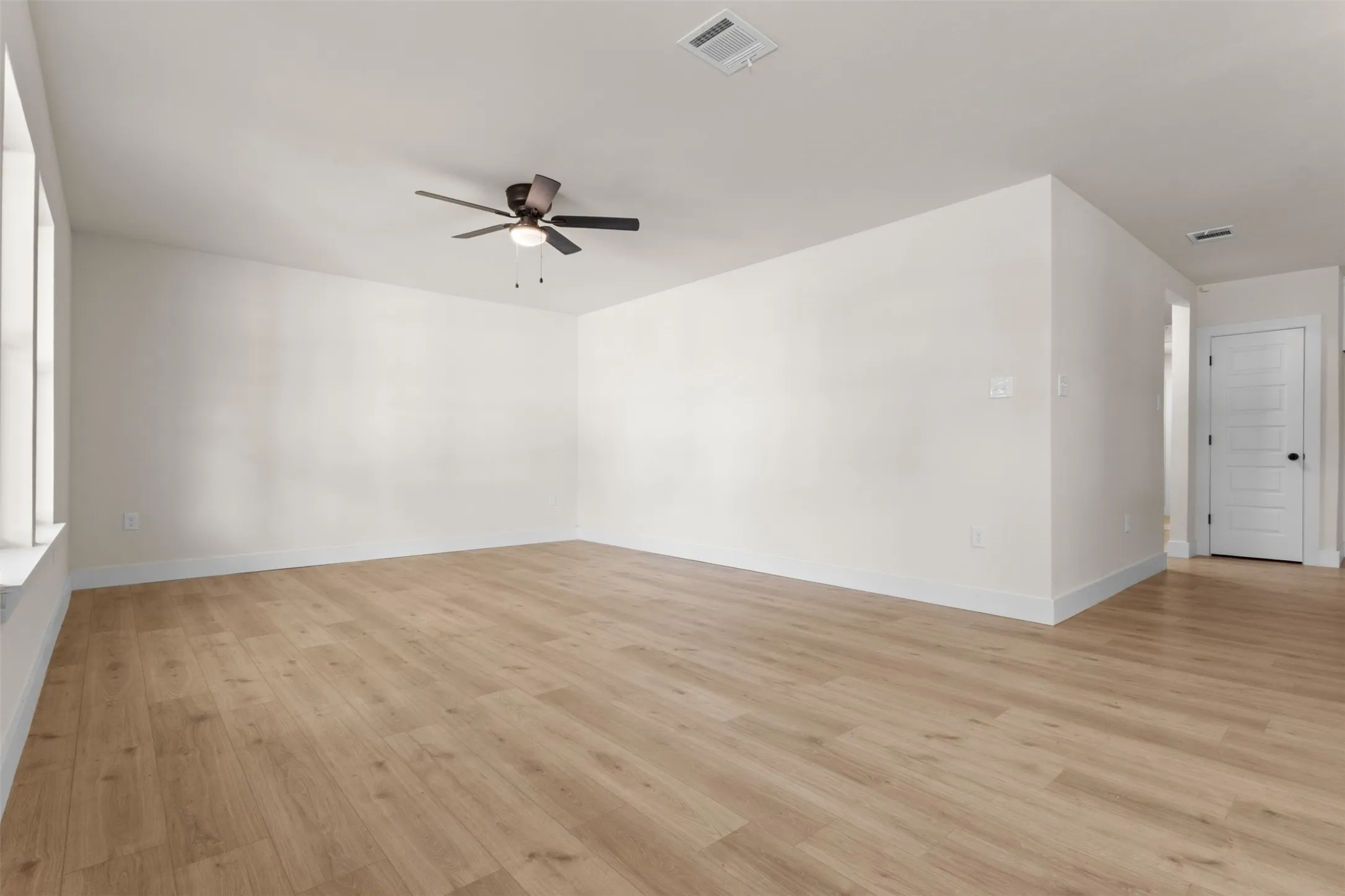 Spacious room featuring wood-finish flooring, white walls, and a ceiling fan
