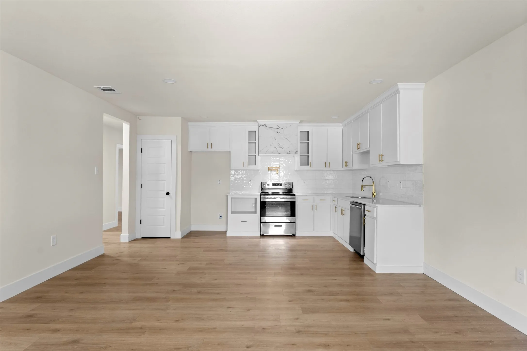 Open-concept kitchen featuring white cabinetry, stainless steel appliances, marble-patterned backsplash, gold-tone hardware, and wood-finish flooring