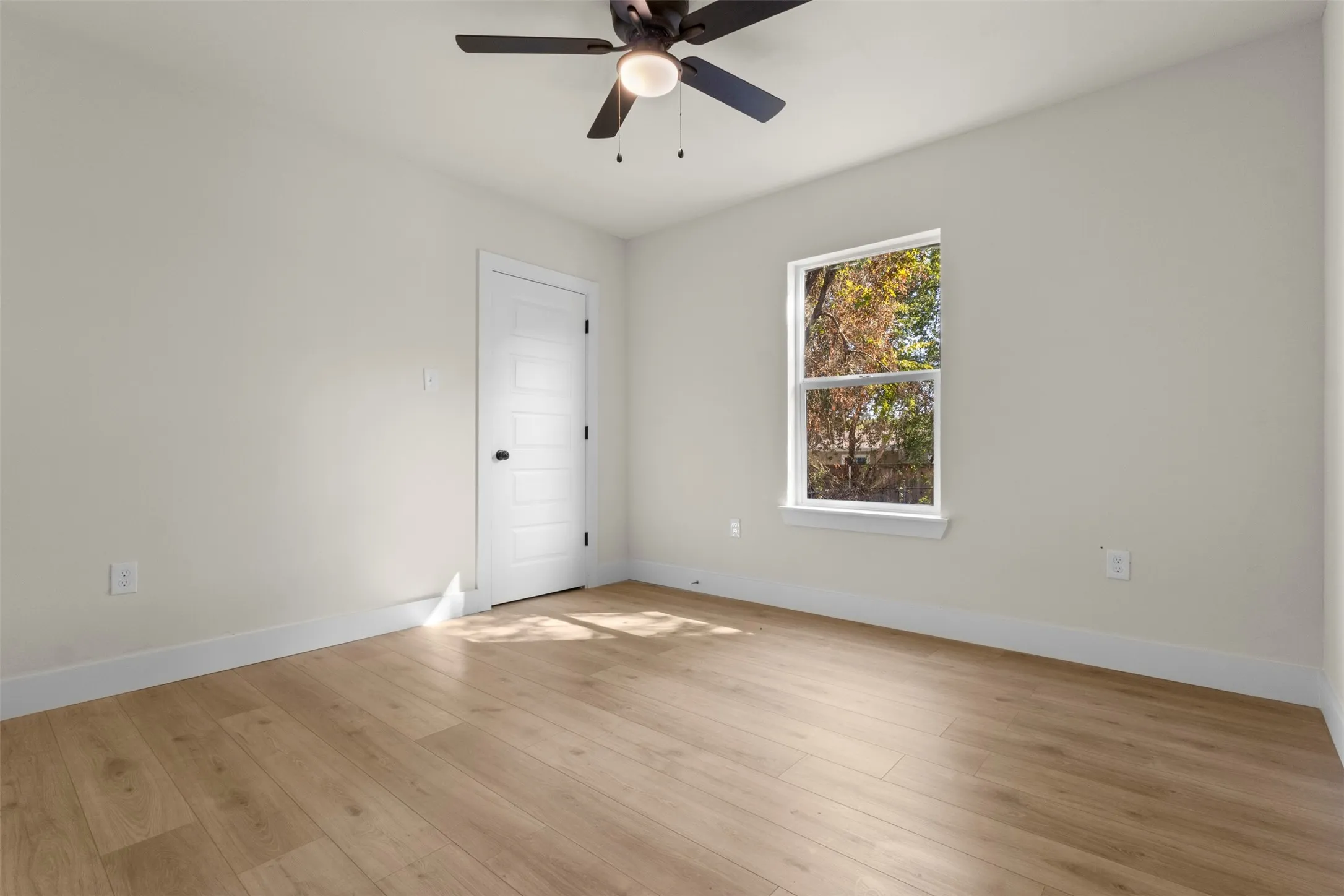 Wood-finish flooring throughout, bright window, ceiling fan with integrated lighting, and a paneled interior door