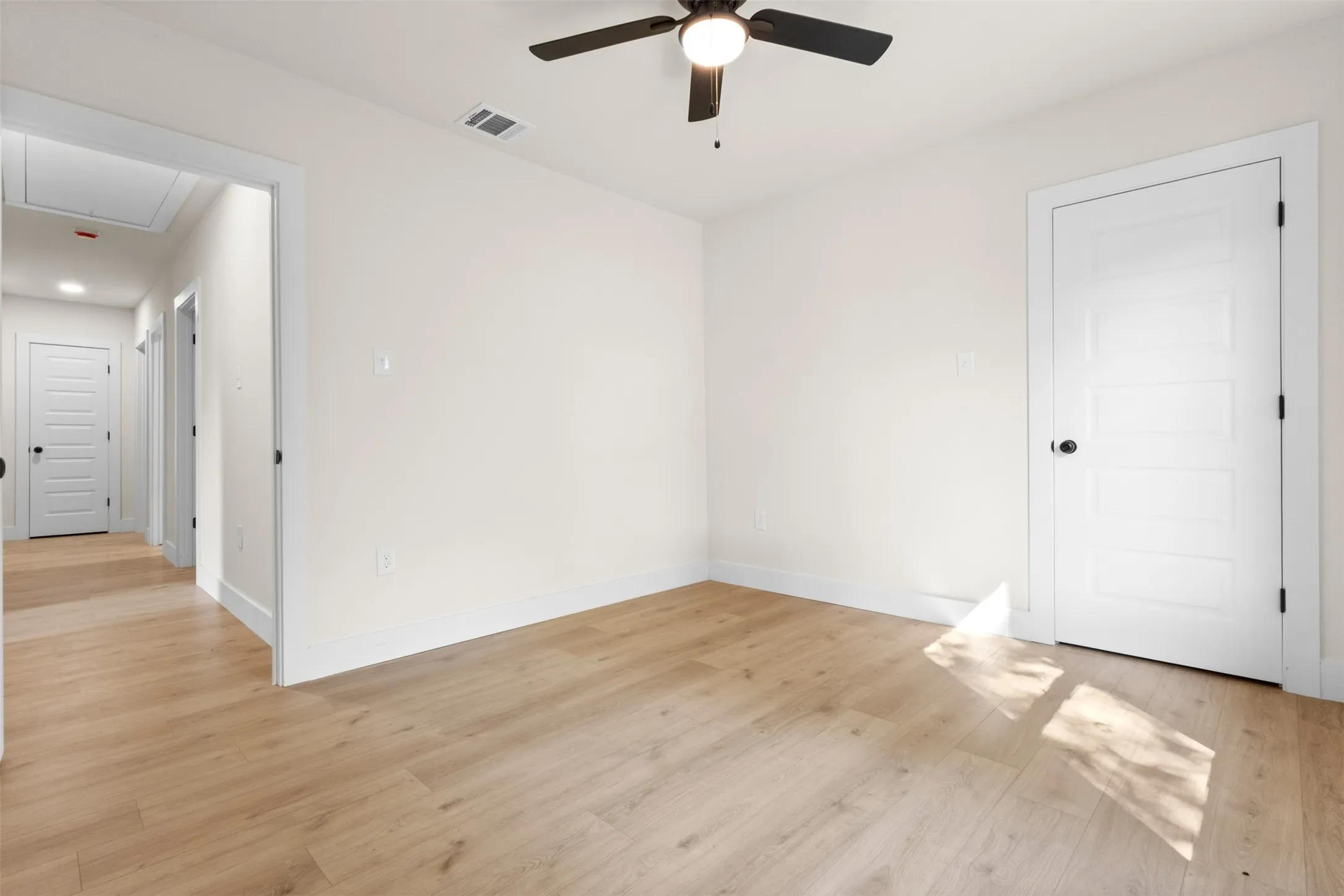 Light wood-finish flooring, white walls, modern five-panel interior doors, and a ceiling fan with integrated lighting