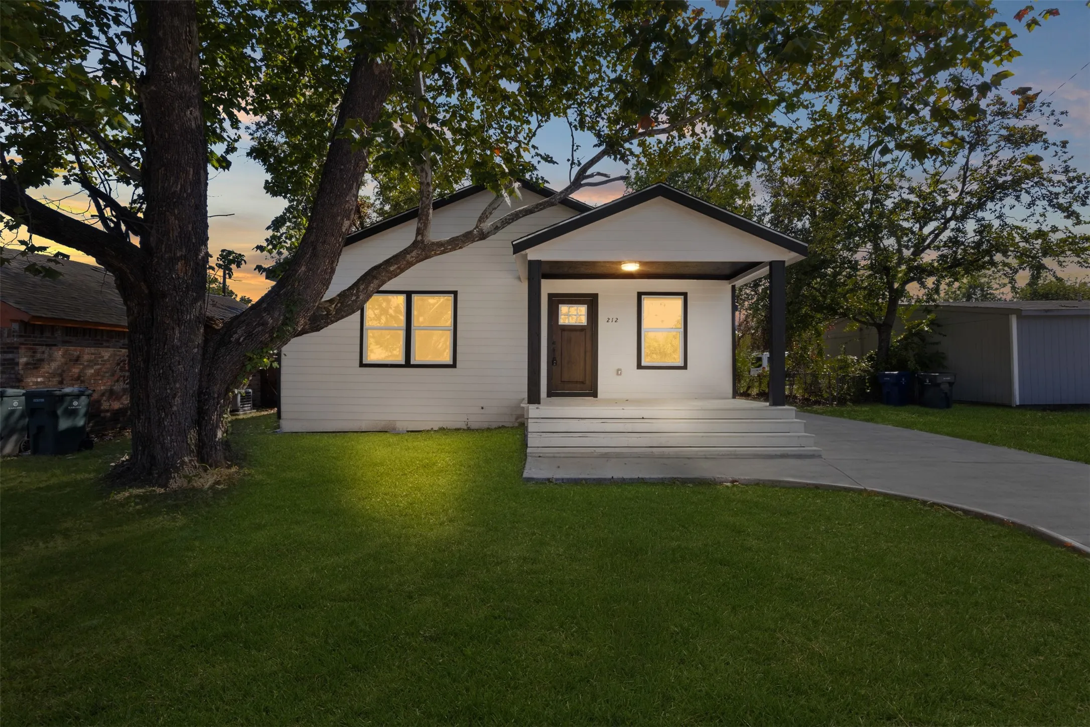 White siding exterior with a dark trim roofline, covered front porch, concrete steps, and a concrete pathway