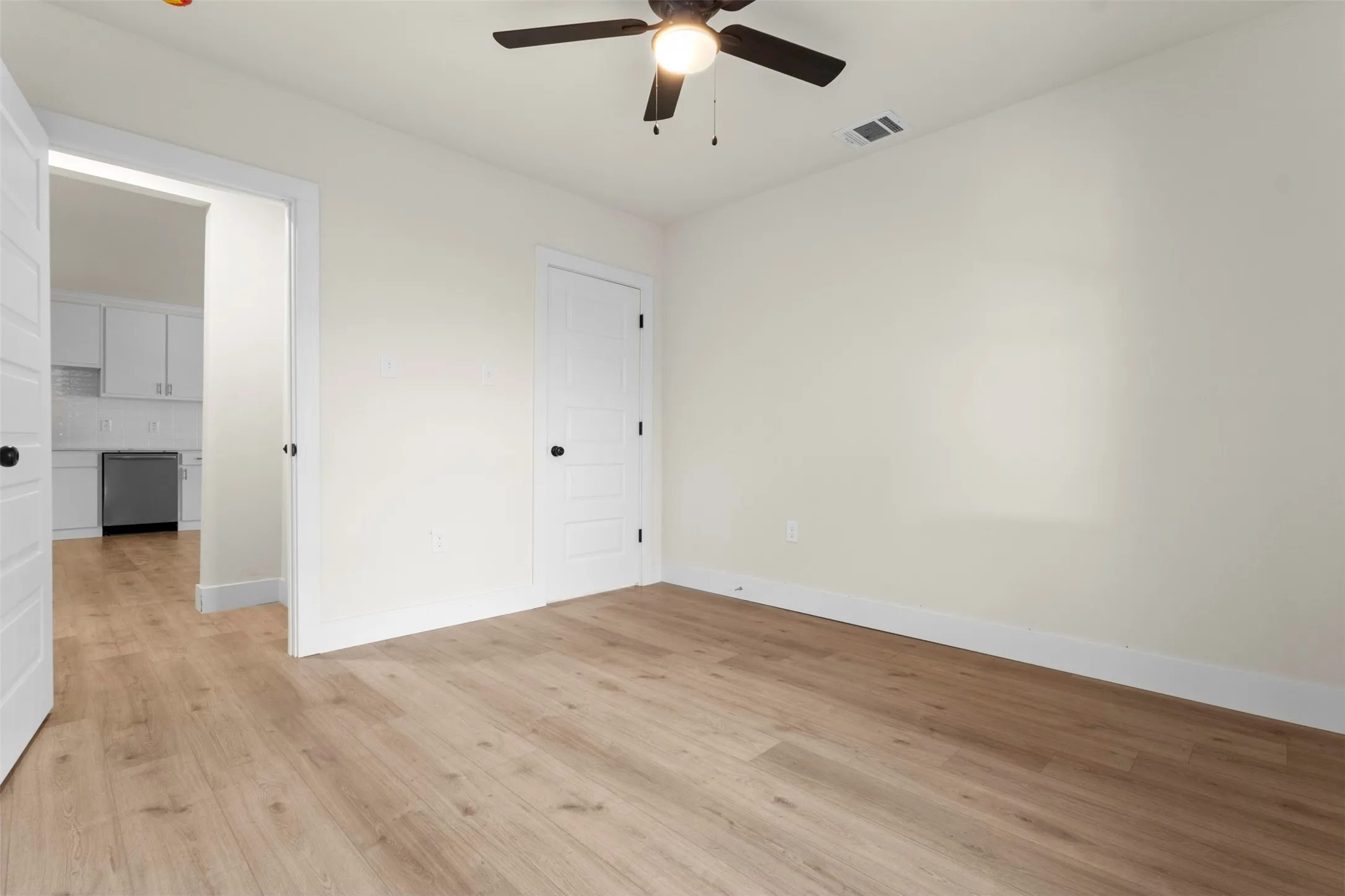Wood-finish flooring, ceiling fan, white interior doors with black hardware, white walls, and a recessed doorway