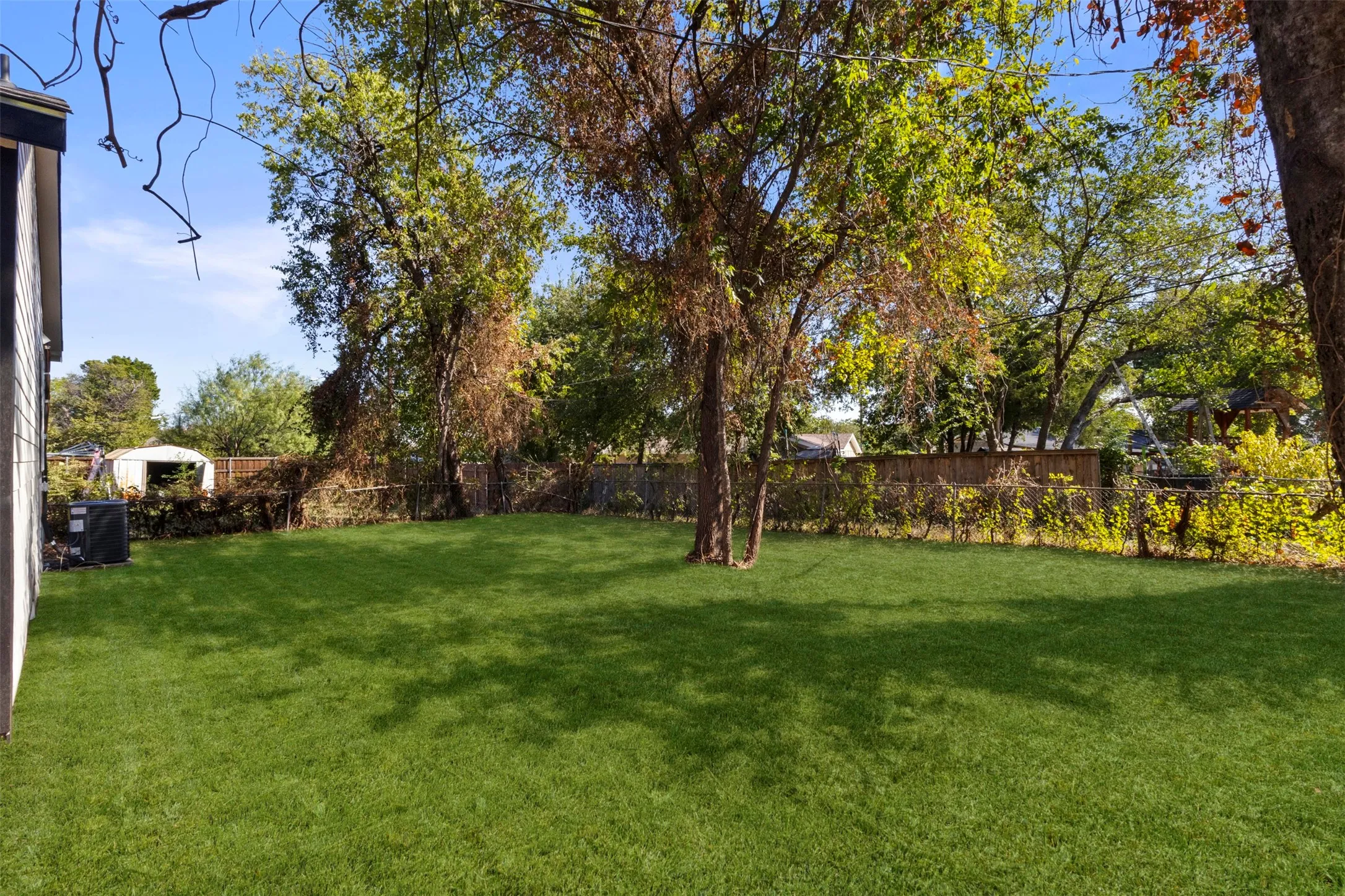 Expansive grassy yard with mature trees and a privacy fence